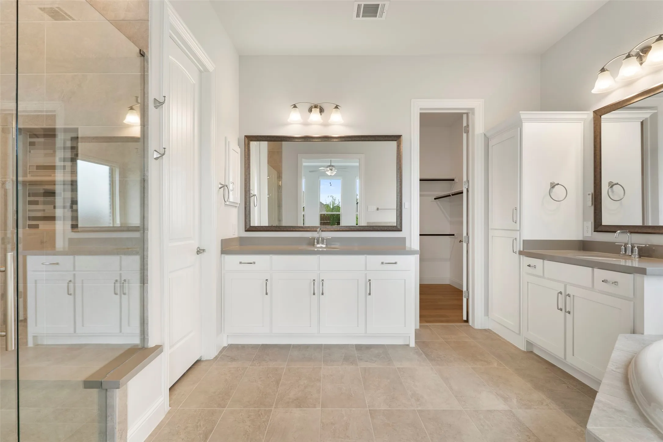 Spacious bathroom featuring twin vanity sinks, extensive white cabinetry, and a large walk-in shower with a built-in bench