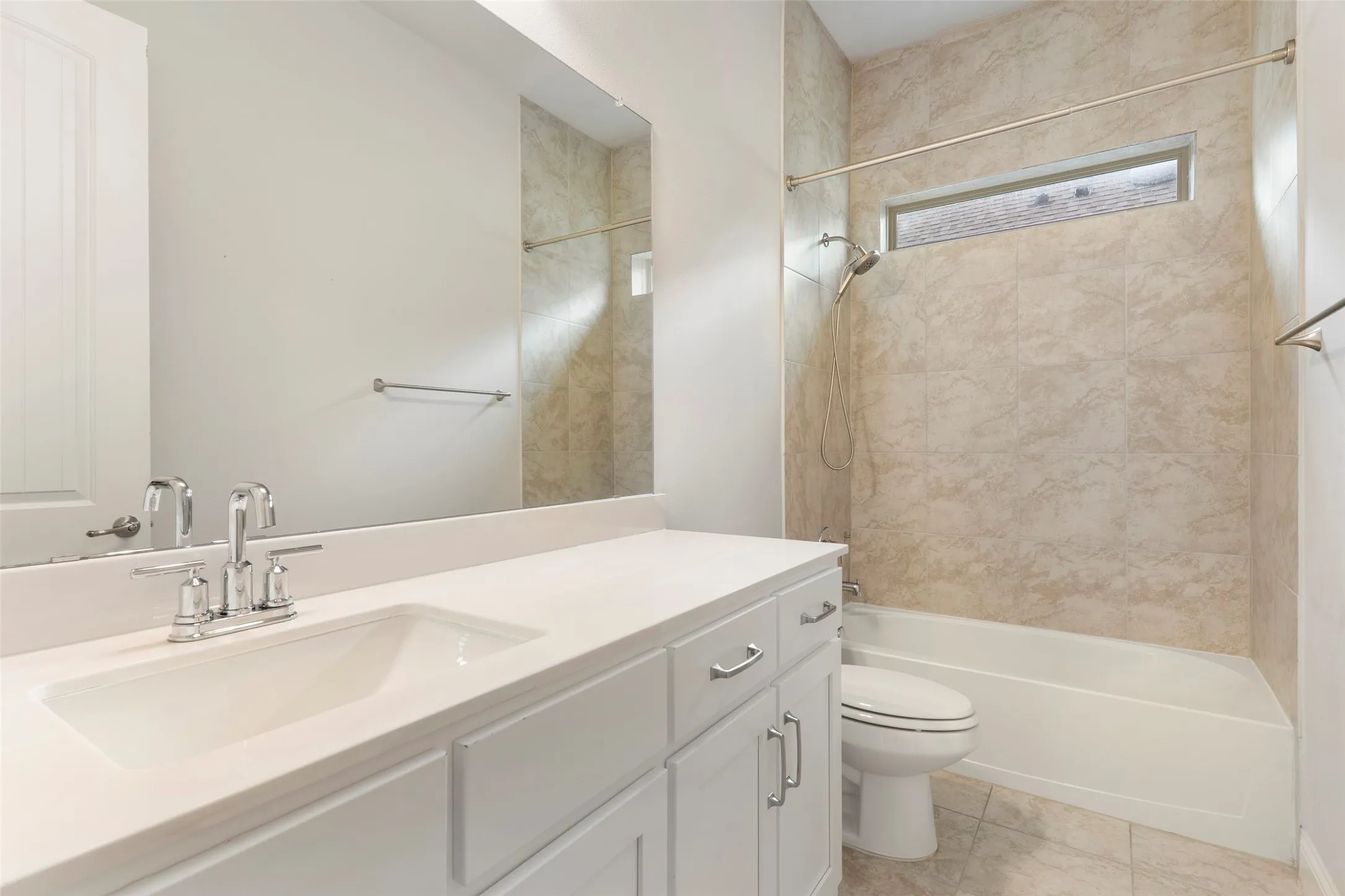 Bathroom featuring white cabinetry, an integrated sink with a chrome faucet, a large vanity mirror, and a bathtub with a tiled surround