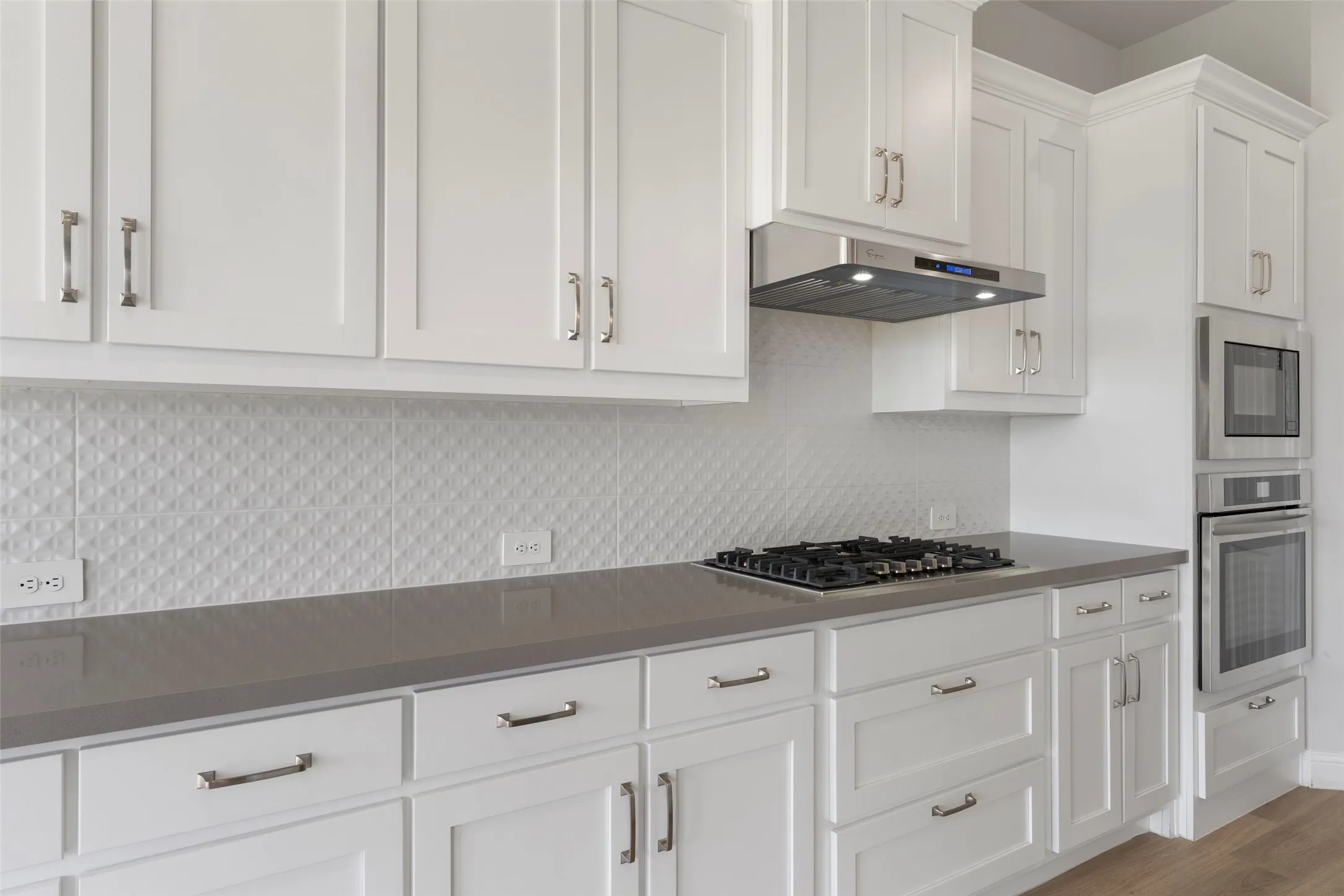 Contemporary kitchen featuring white shaker cabinetry, a patterned tile backsplash, gray countertops, a stainless steel gas cooktop, and built-in stainless steel appliances