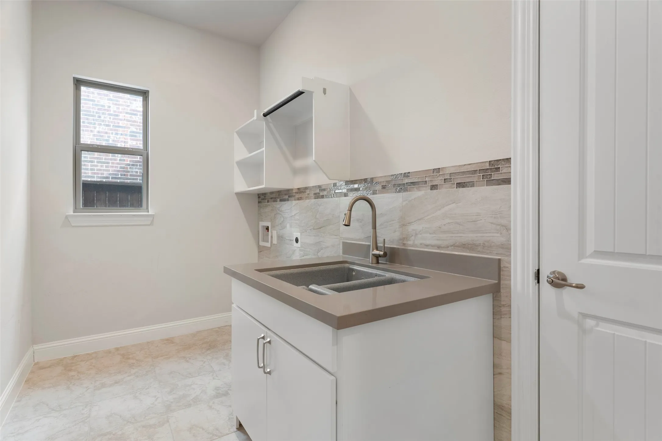 Utility sink with a gooseneck faucet, set within a white cabinet with a stone-finish countertop