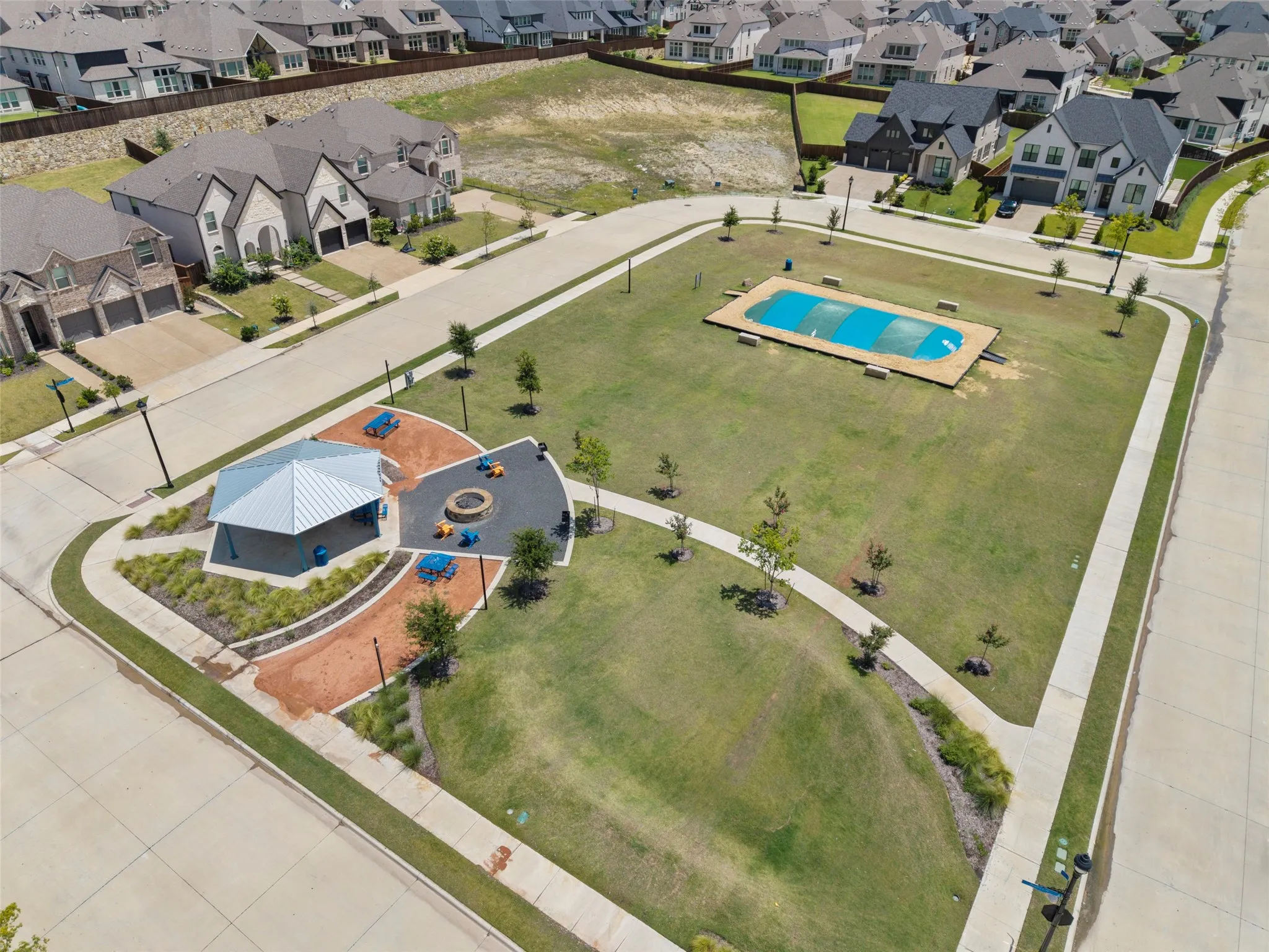 Central community green space featuring a covered pavilion, integrated fire pit area, and a rectangular swimming pool with a blue cover
