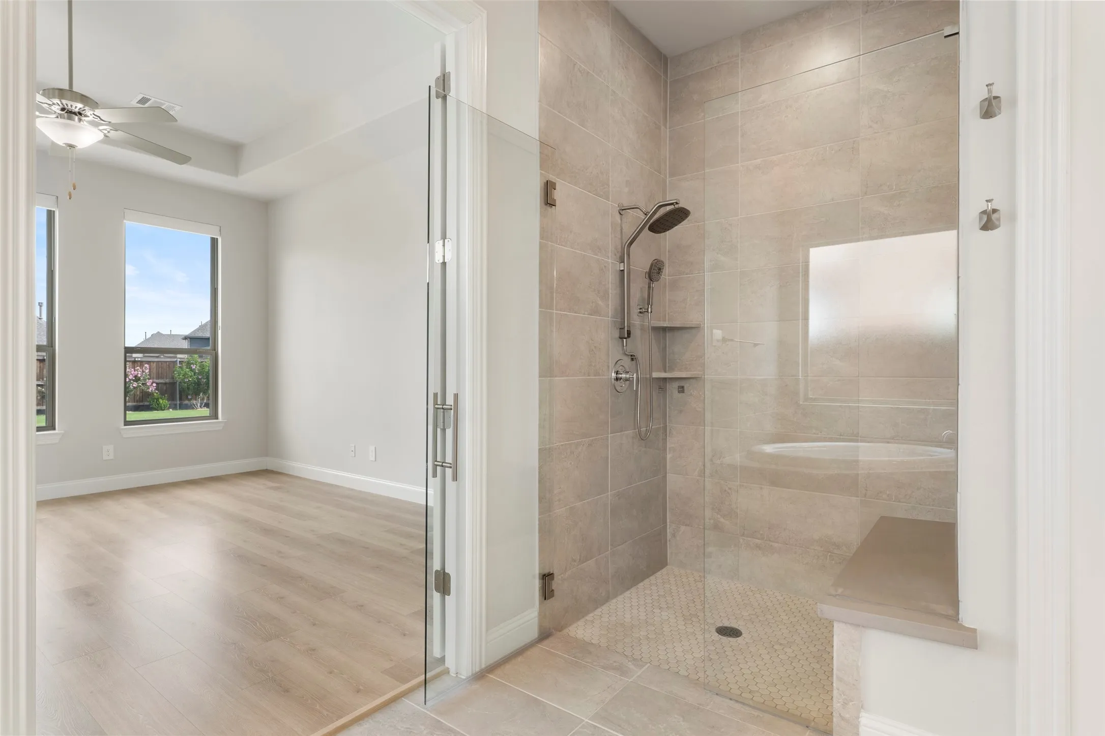 Expansive en-suite bath featuring a glass-enclosed shower with full tile surround, integrated shower bench, and a built-in niche