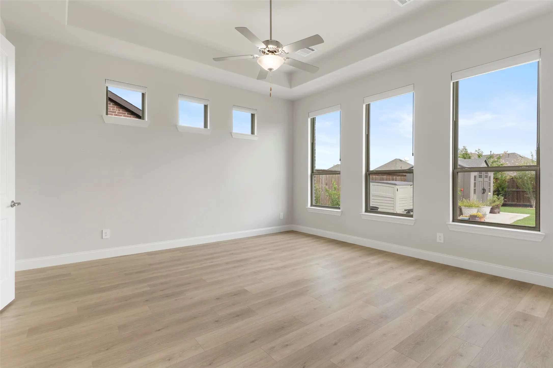 Spacious room featuring wood-finish flooring, a tray ceiling, and a ceiling fan with integrated lighting