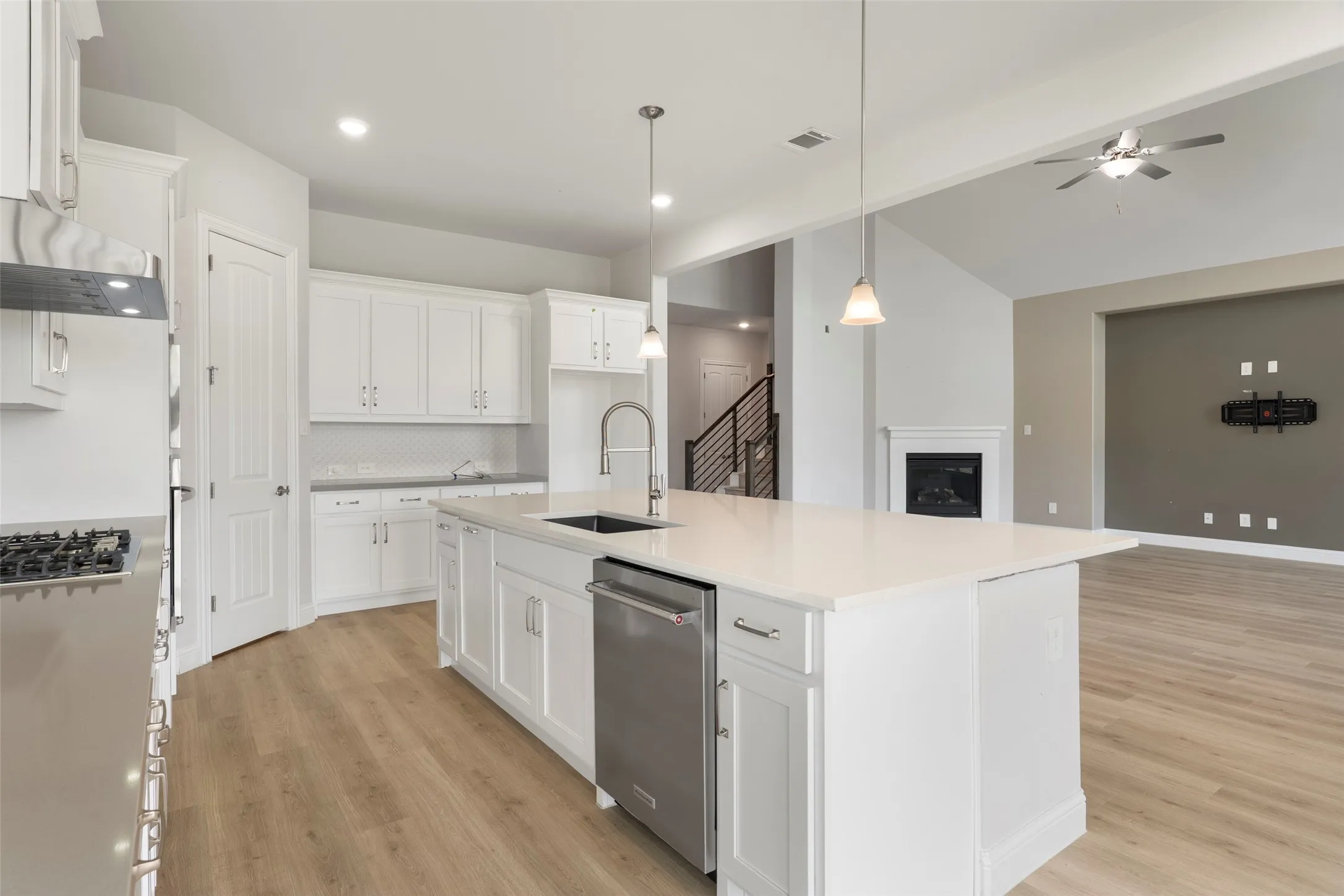 Gourmet kitchen featuring a large island with a sink, stainless steel dishwasher, pendant lighting, and abundant white cabinetry