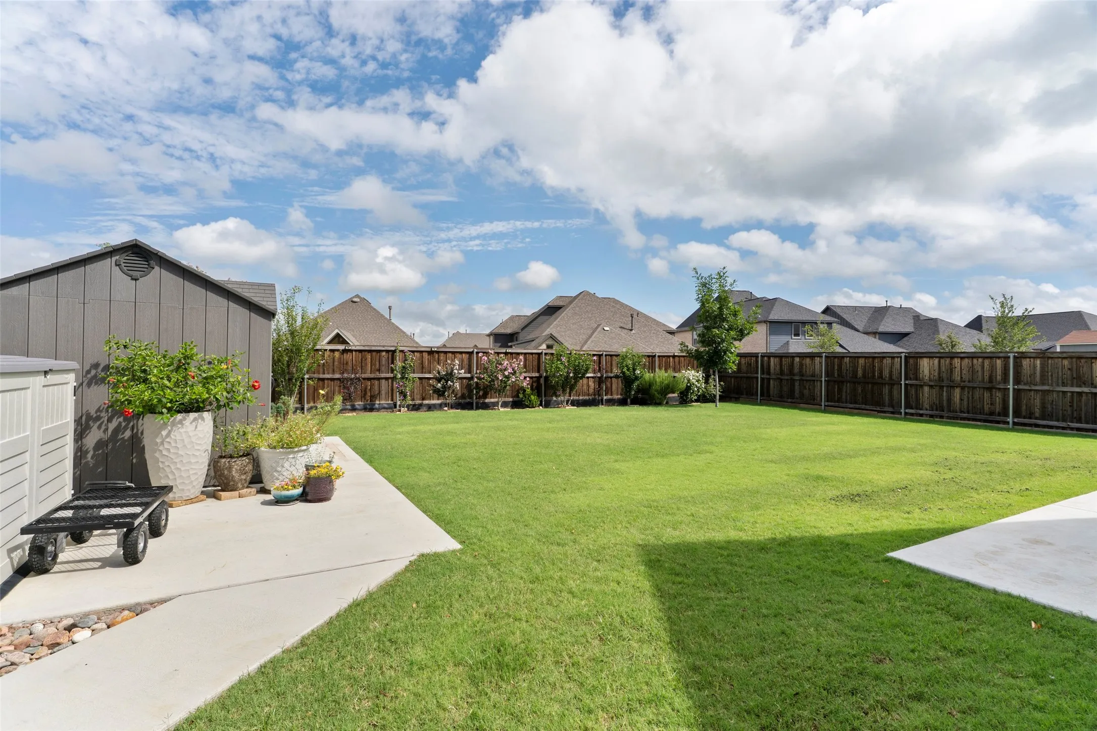Expansive backyard featuring a large green lawn, concrete patio, and privacy fencing