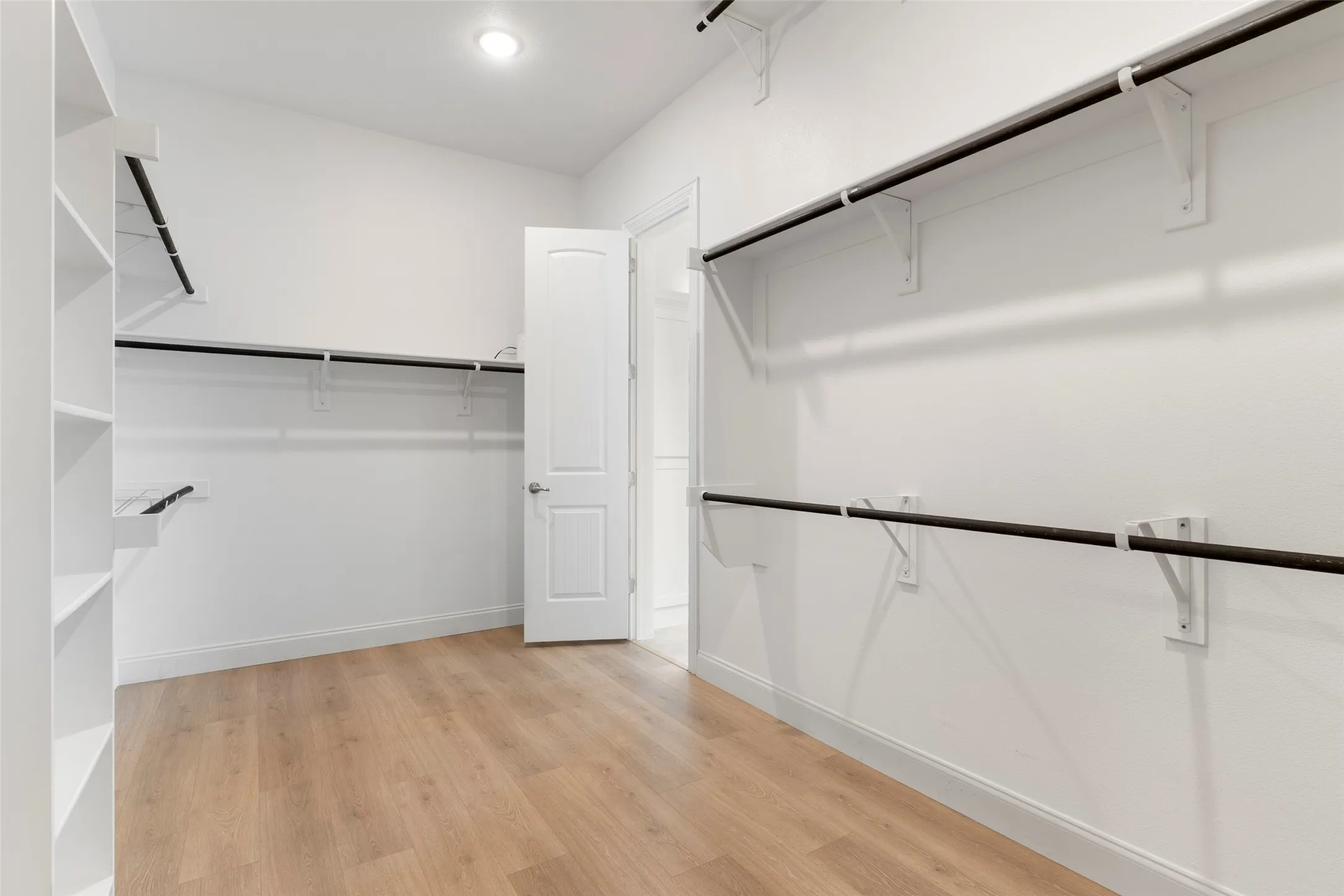 Spacious walk-in closet featuring light wood-finish flooring, white walls, and built-in shelving