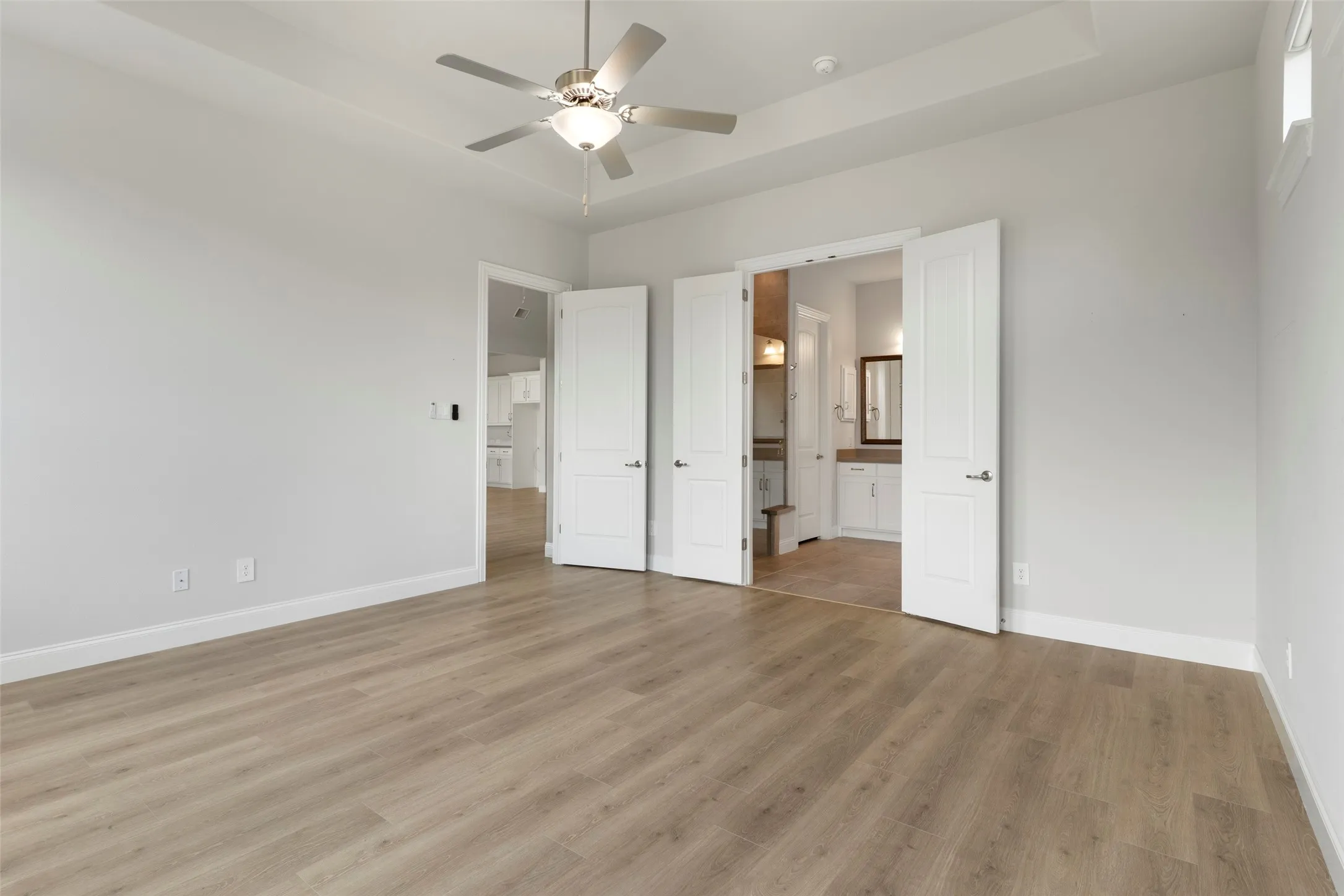 Spacious room featuring wood-finish flooring, light grey walls, and a ceiling fan with integrated lighting