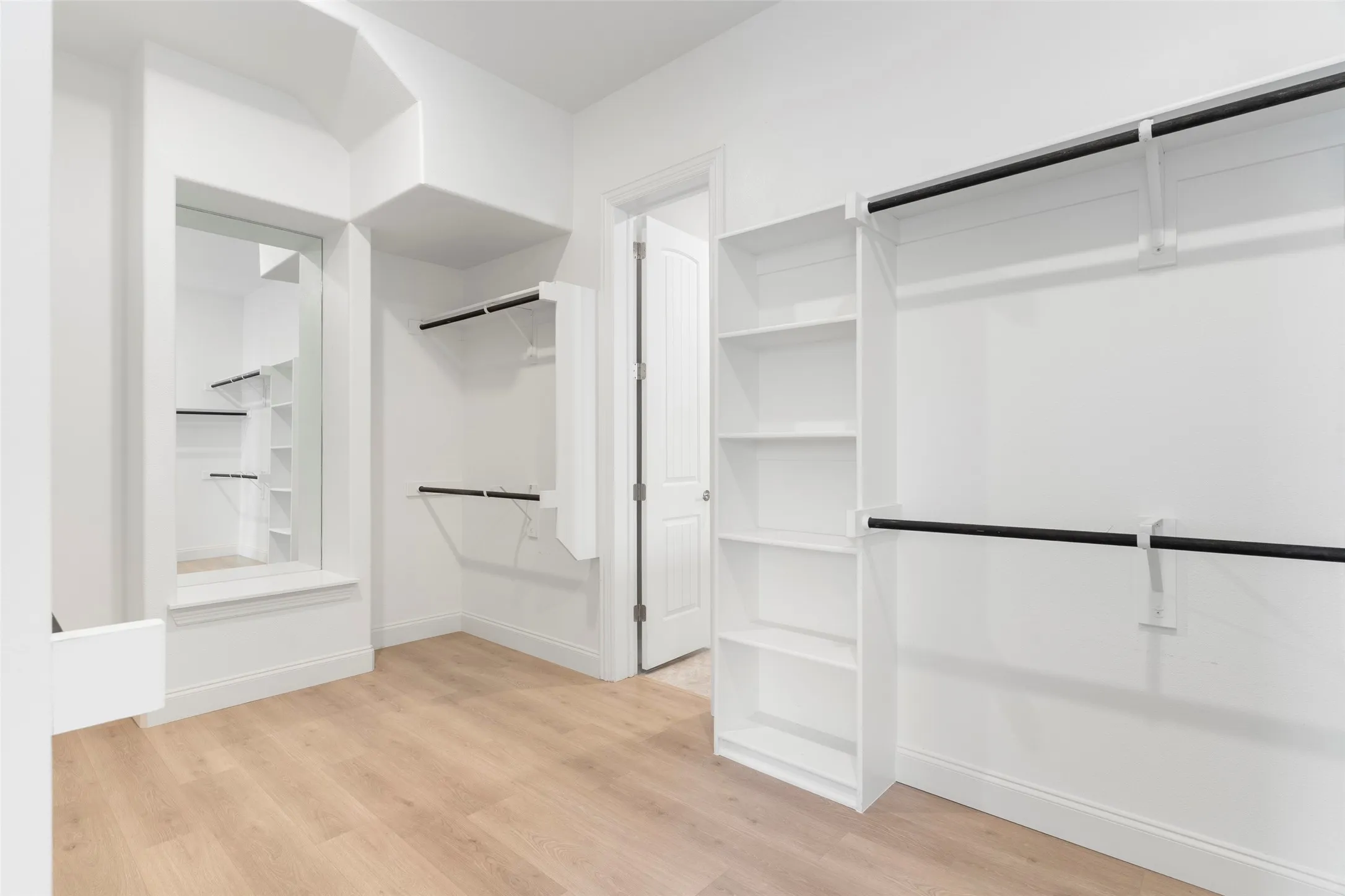 Custom closet system featuring ample shelving, hanging rods, and wood-finish flooring