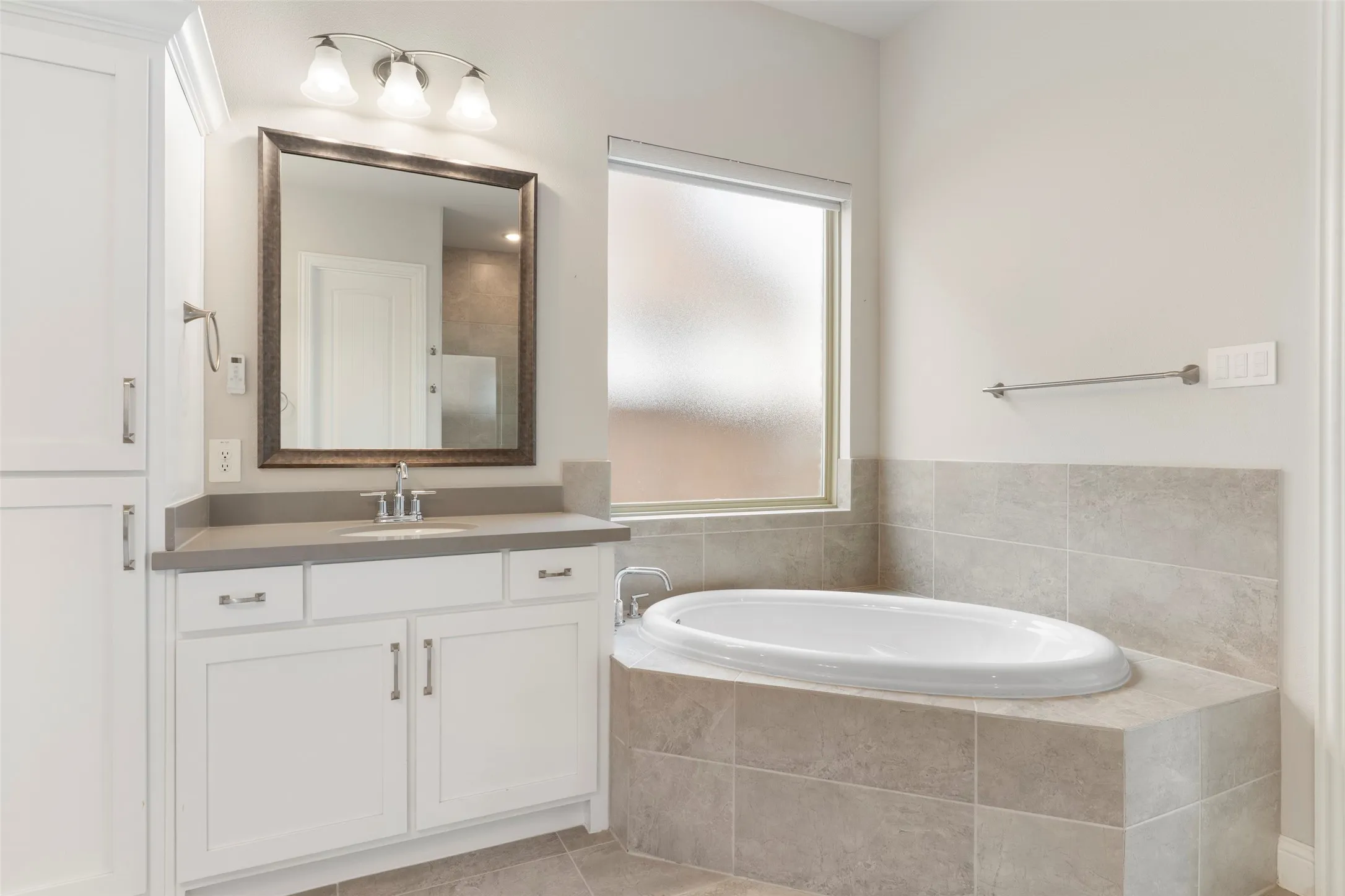 Bathroom featuring a built-in soaking tub with tile surround, a frosted window, and a single vanity with a gray countertop