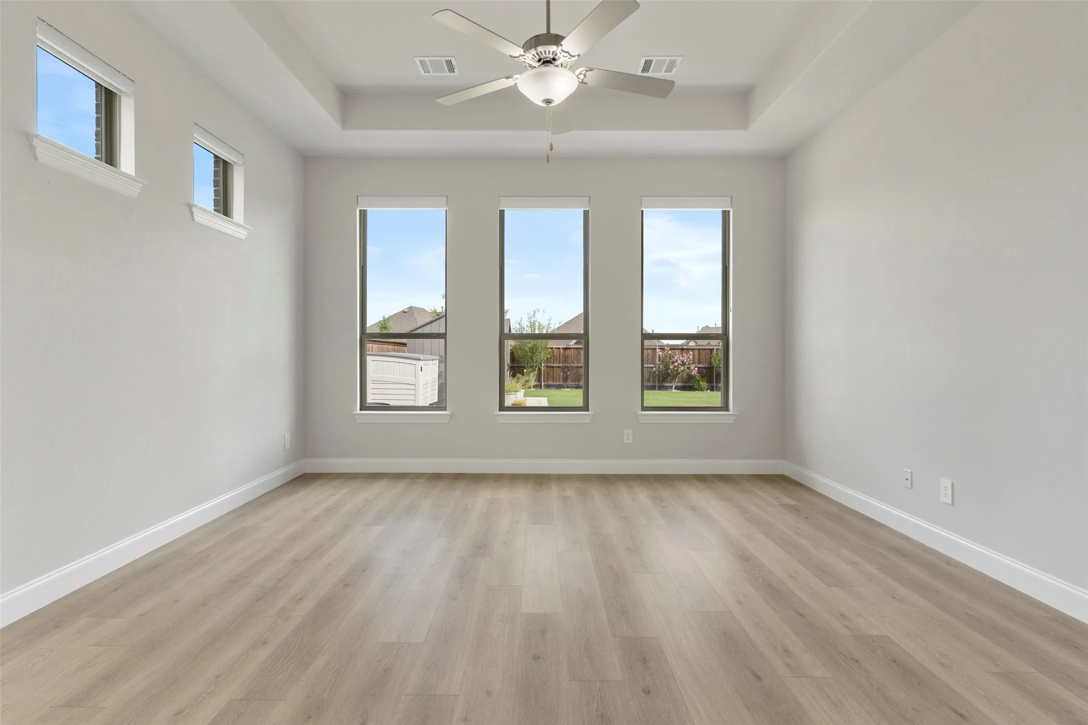 Spacious room featuring wood-finish flooring, a tray ceiling, and a ceiling fan