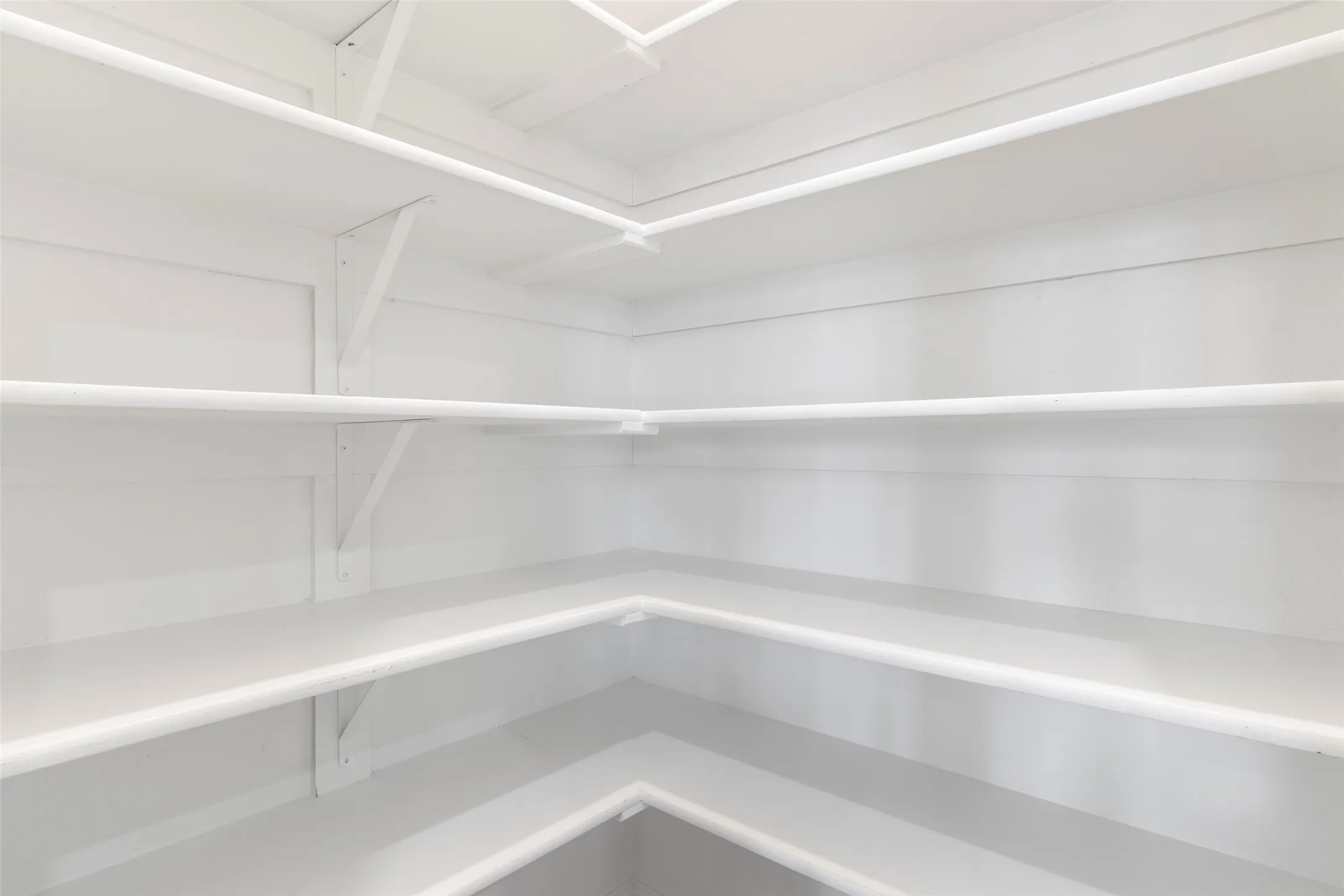 Corner pantry featuring multiple white shelving units and support brackets