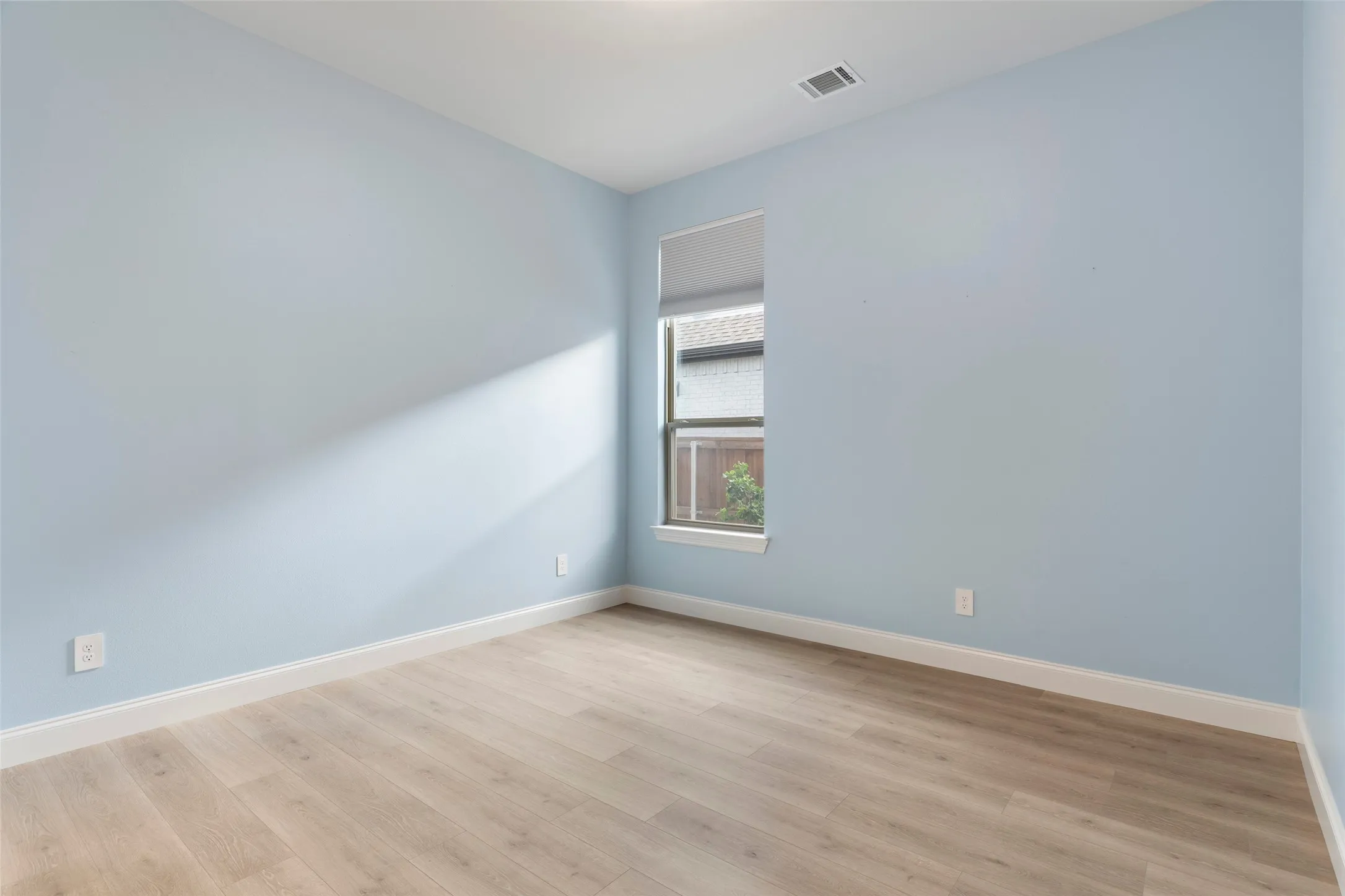 Room featuring light wood-finish flooring, white baseboards, a single window, and a ceiling-mounted HVAC vent
