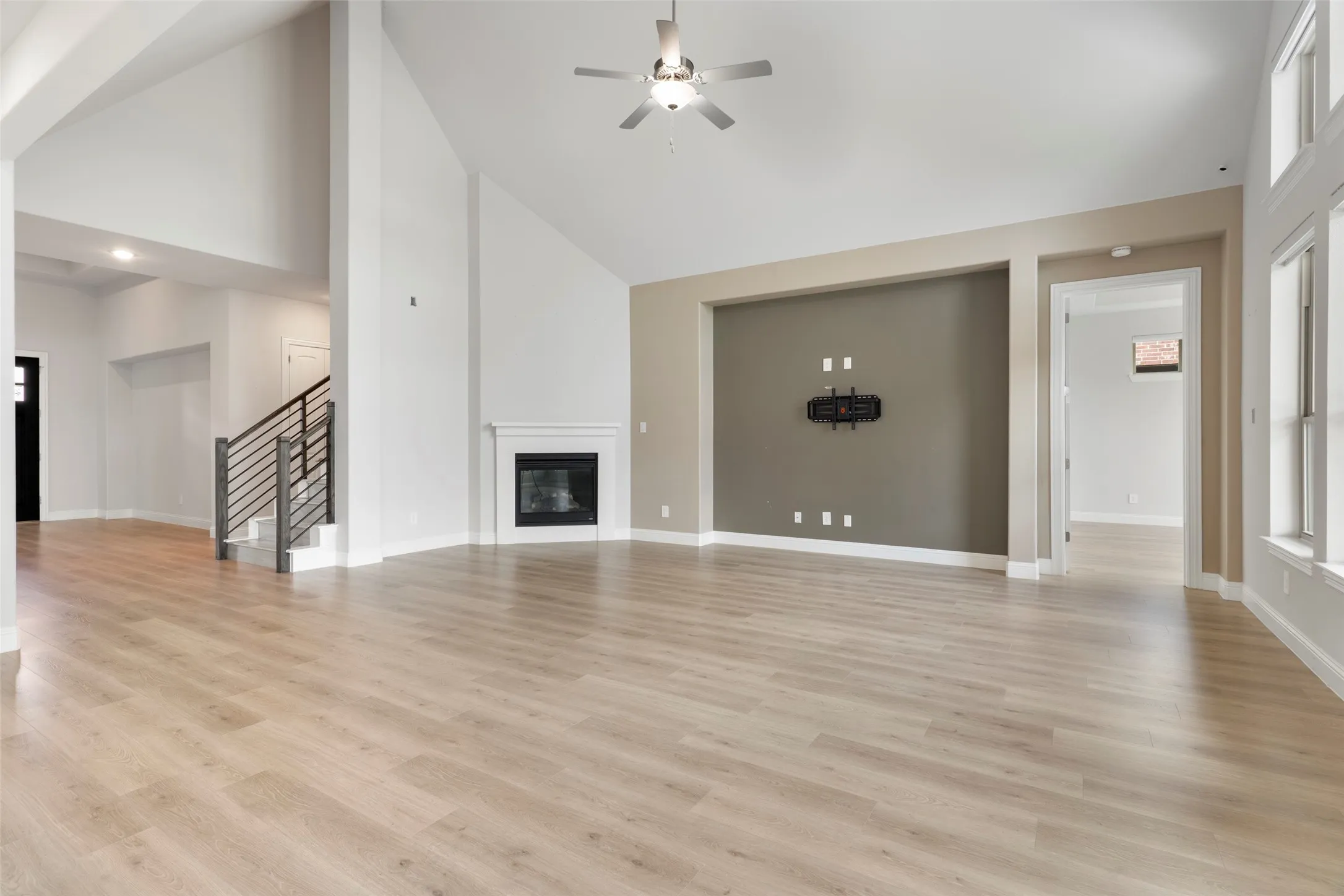 Spacious living area featuring light wood-finish flooring, vaulted ceilings, a built-in fireplace with white mantle, and a recessed wall for media