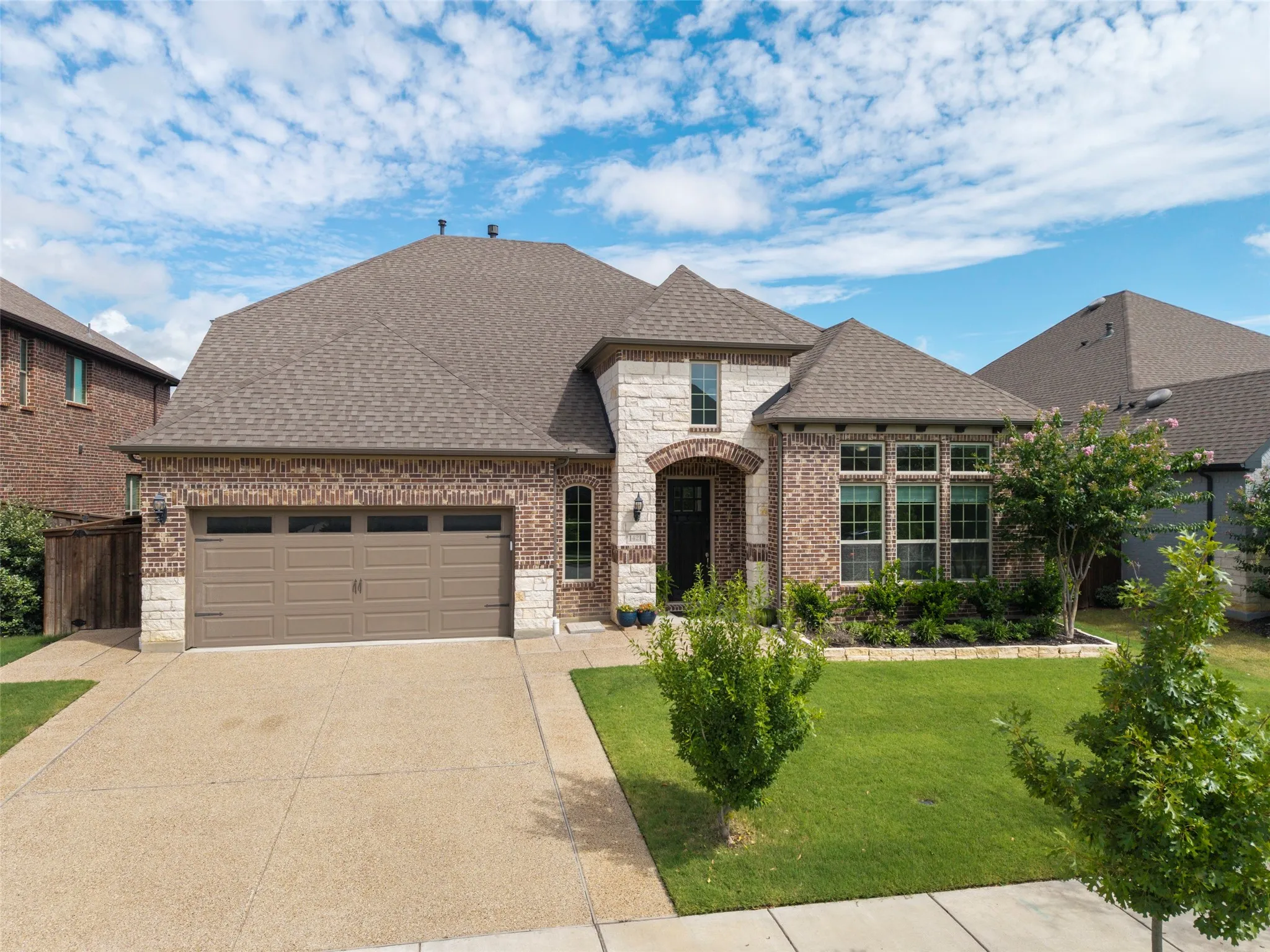 Brick and stone exterior featuring an arched entryway, gabled roofline, and a two-car garage