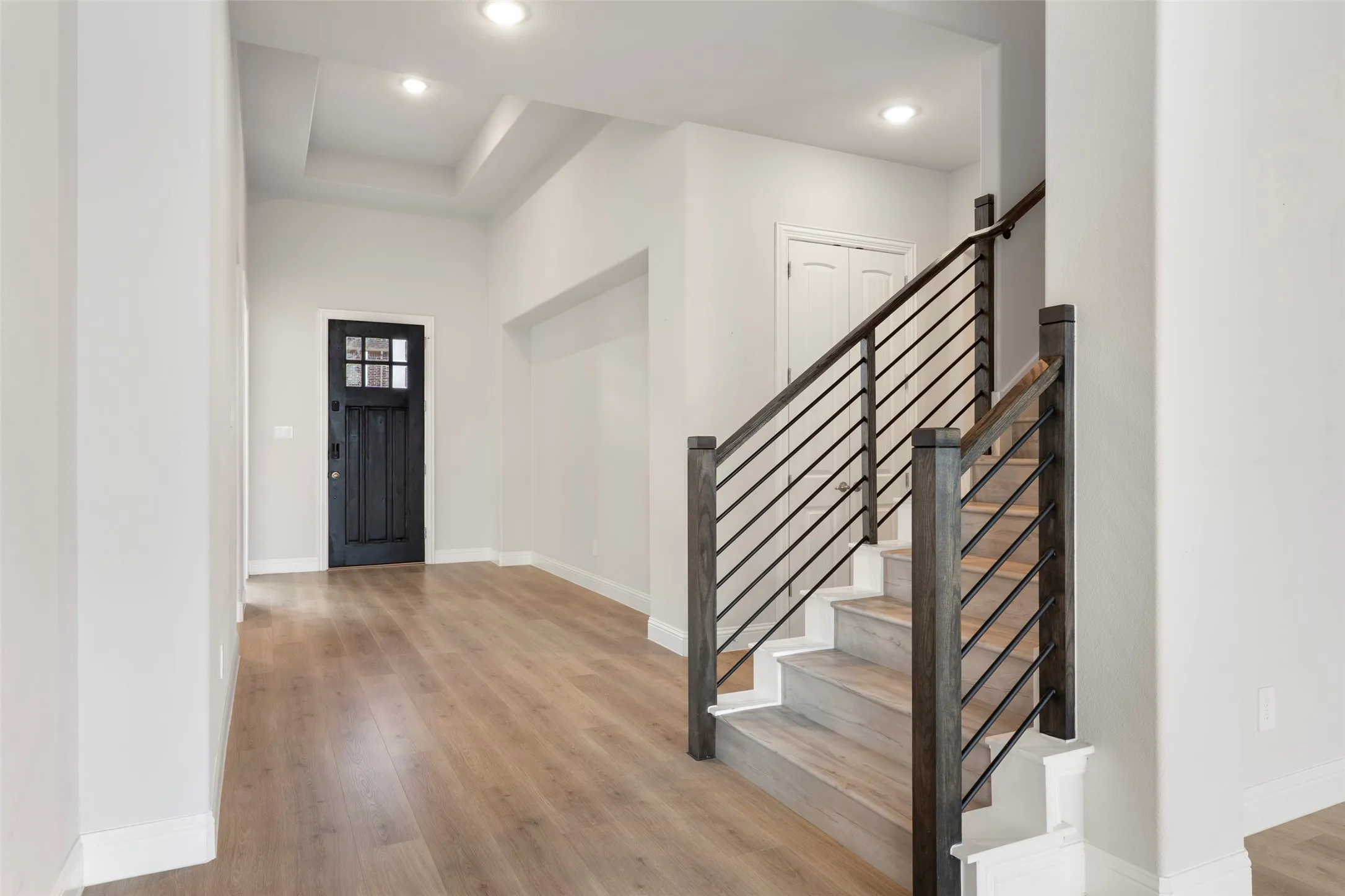 Foyer featuring a dark wood entry door with glass panels, wood-finish flooring, a tray ceiling with recessed lighting, and a staircase with wood newel posts and horizontal metal balusters