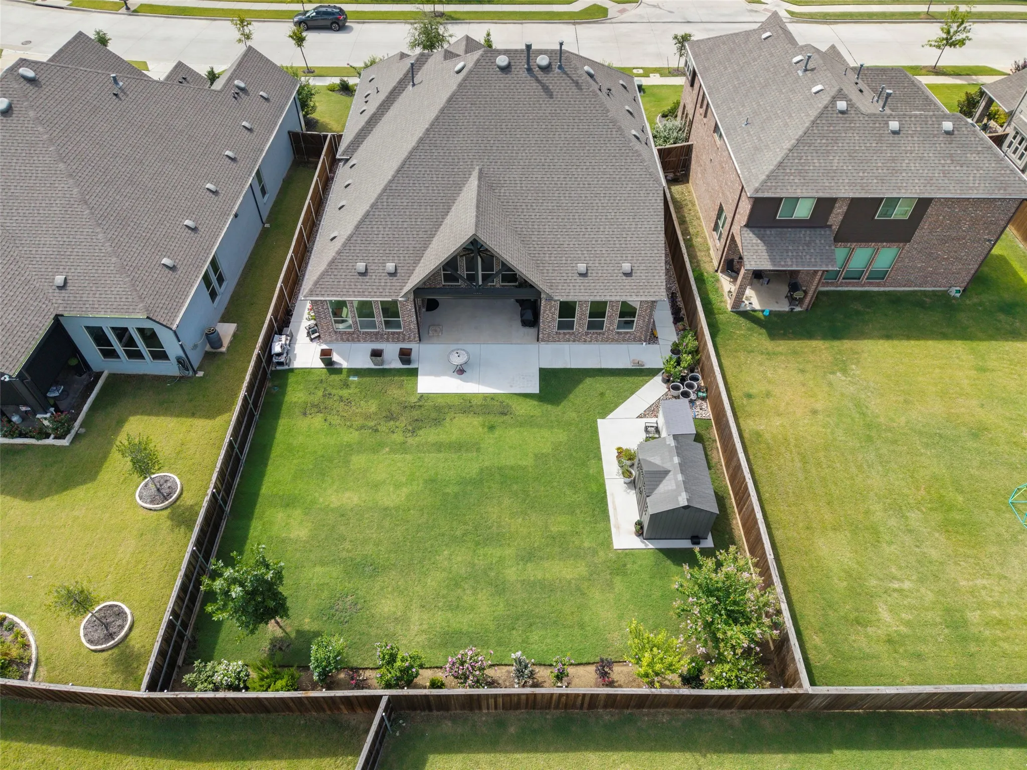 Expansive fenced backyard featuring a manicured lawn, an extended patio, a storage shed on a concrete pad, a mature tree, and perimeter landscaping