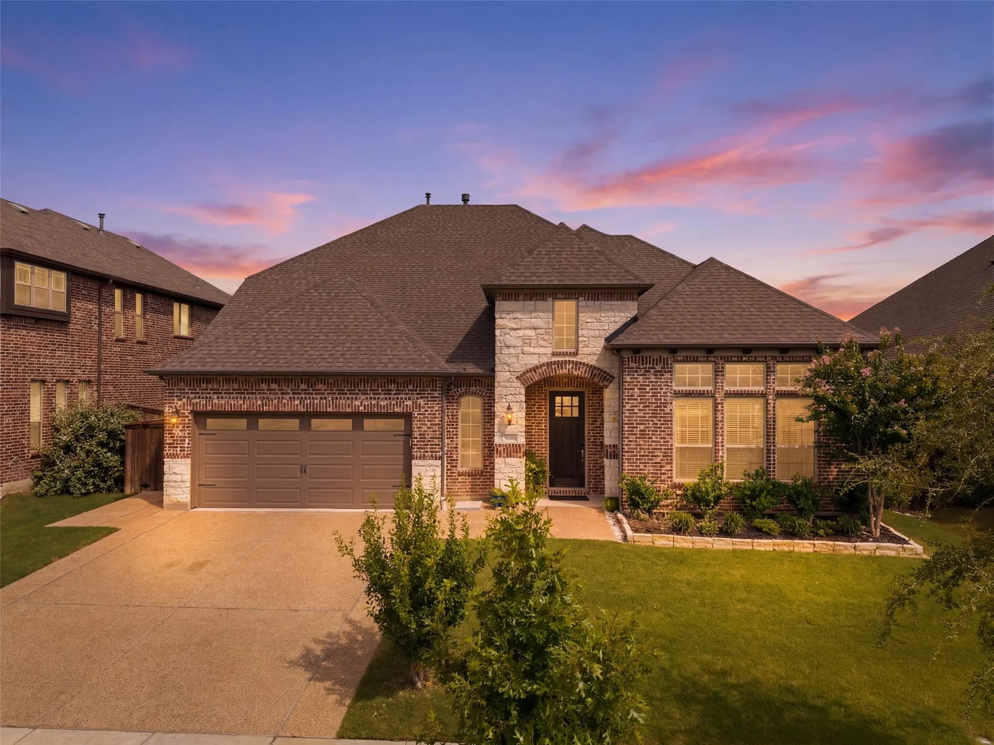 Brick and stone facade residence featuring a two-car garage, established landscaping, arched entryway, and multiple windows