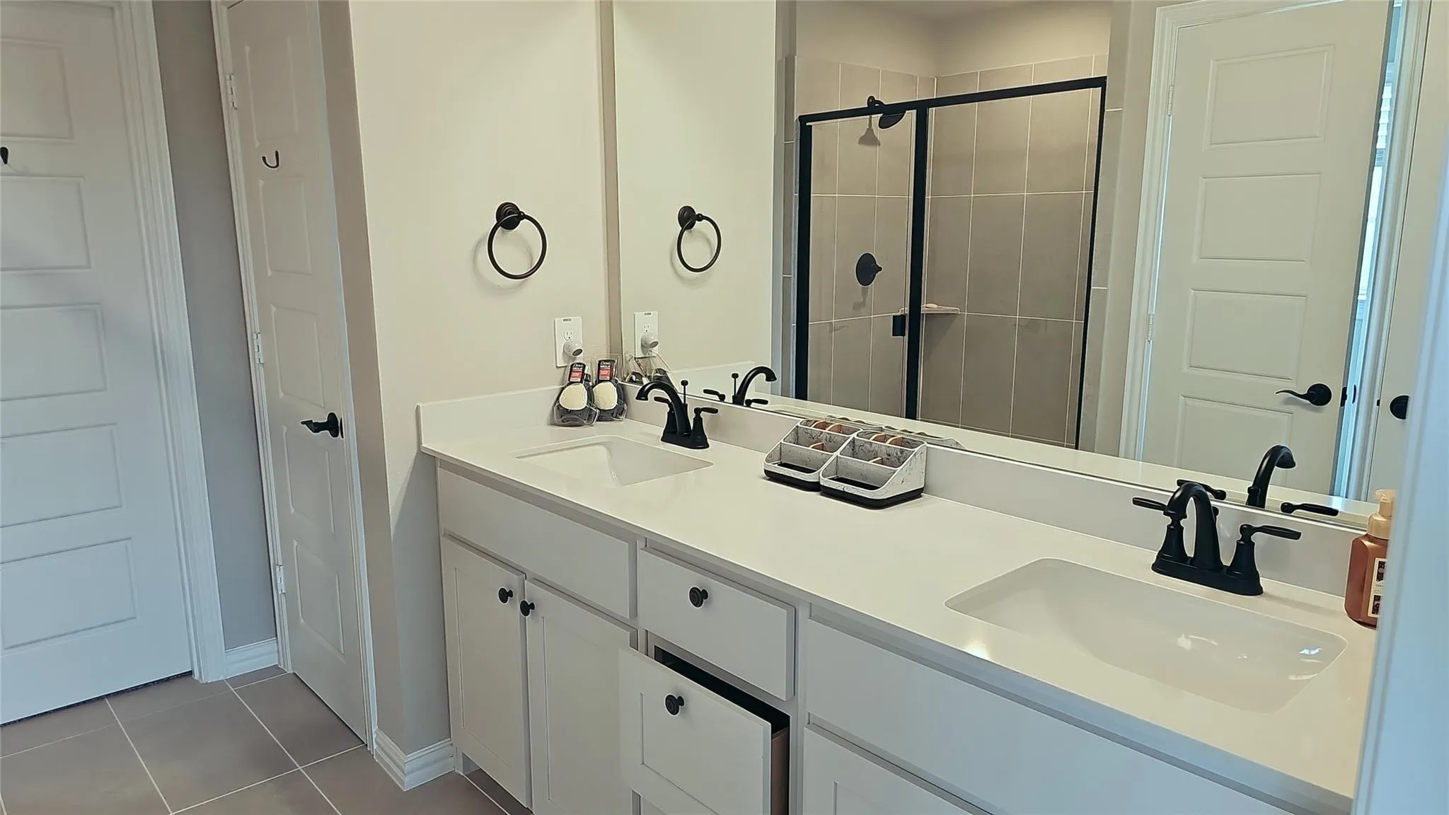 Bathroom vanity featuring dual undermount sinks, white cabinetry with matte black hardware, and an expansive mirror