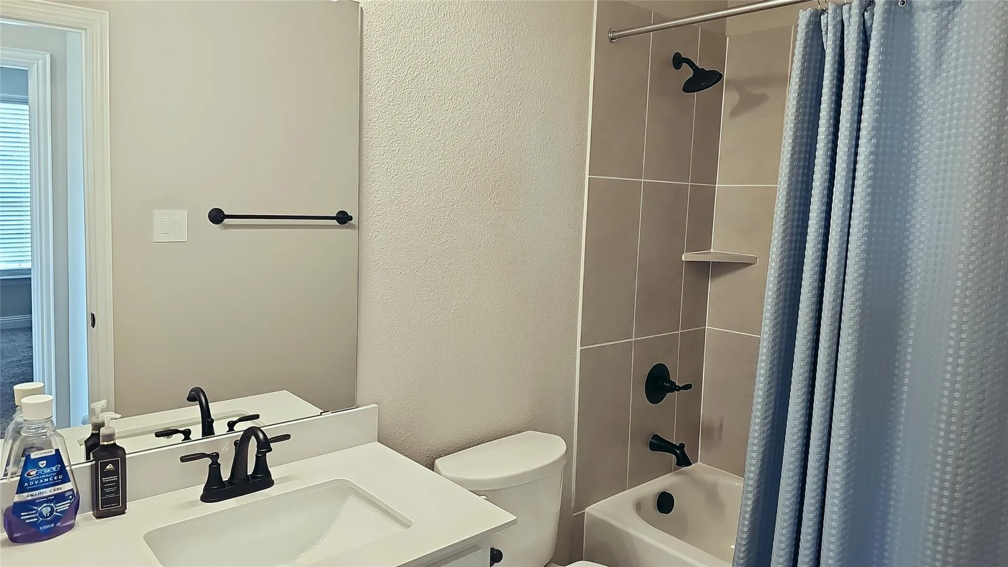 Bathroom featuring a single vanity with an integrated sink and matte black faucet, a full-width mirror, and a tub-shower combination with tiled surround and matte black fixtures