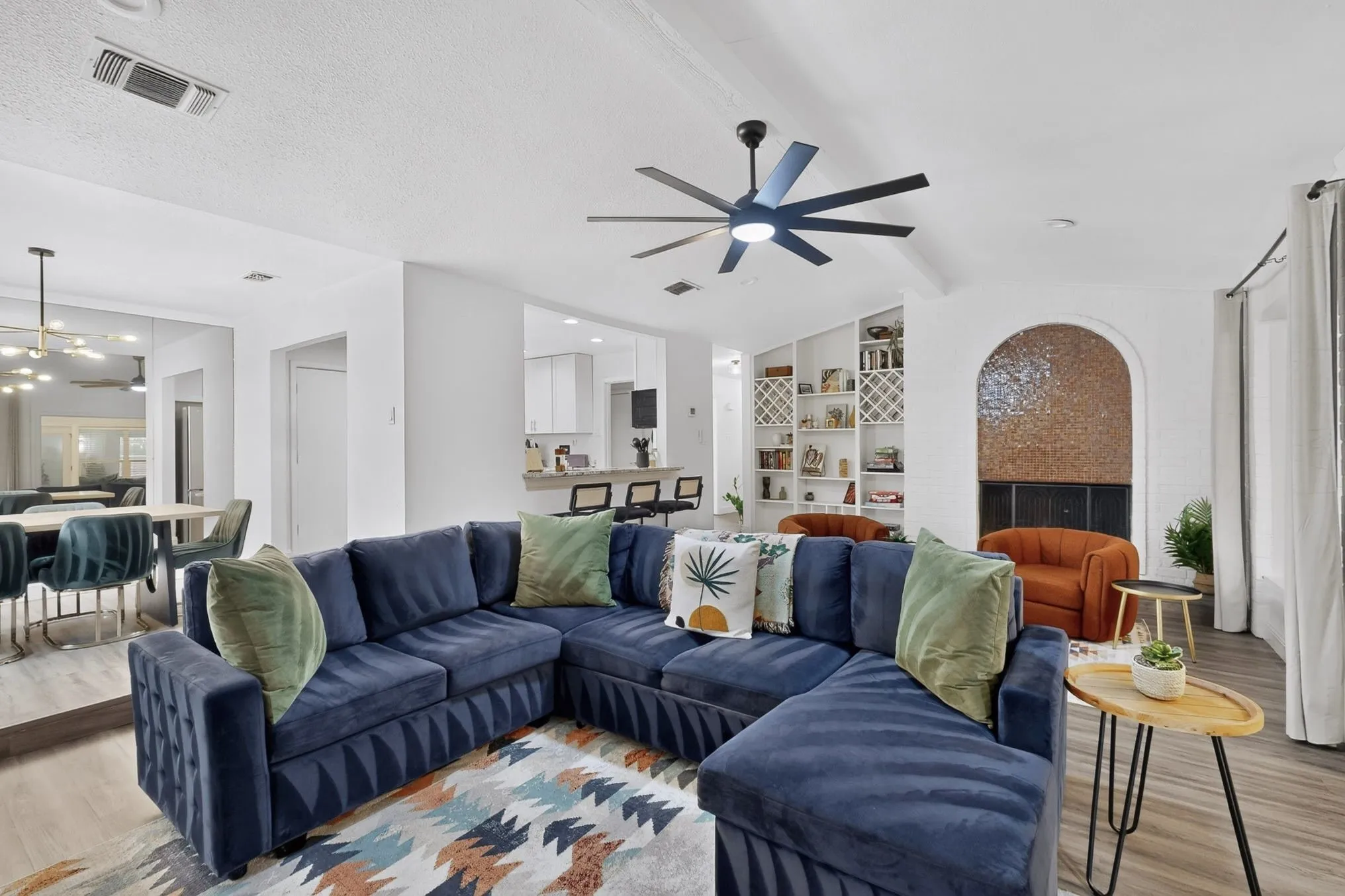 Open-concept living space featuring wood-finish flooring, a modern ceiling fan, recessed lighting, built-in shelving, and an arched alcove with mosaic tile