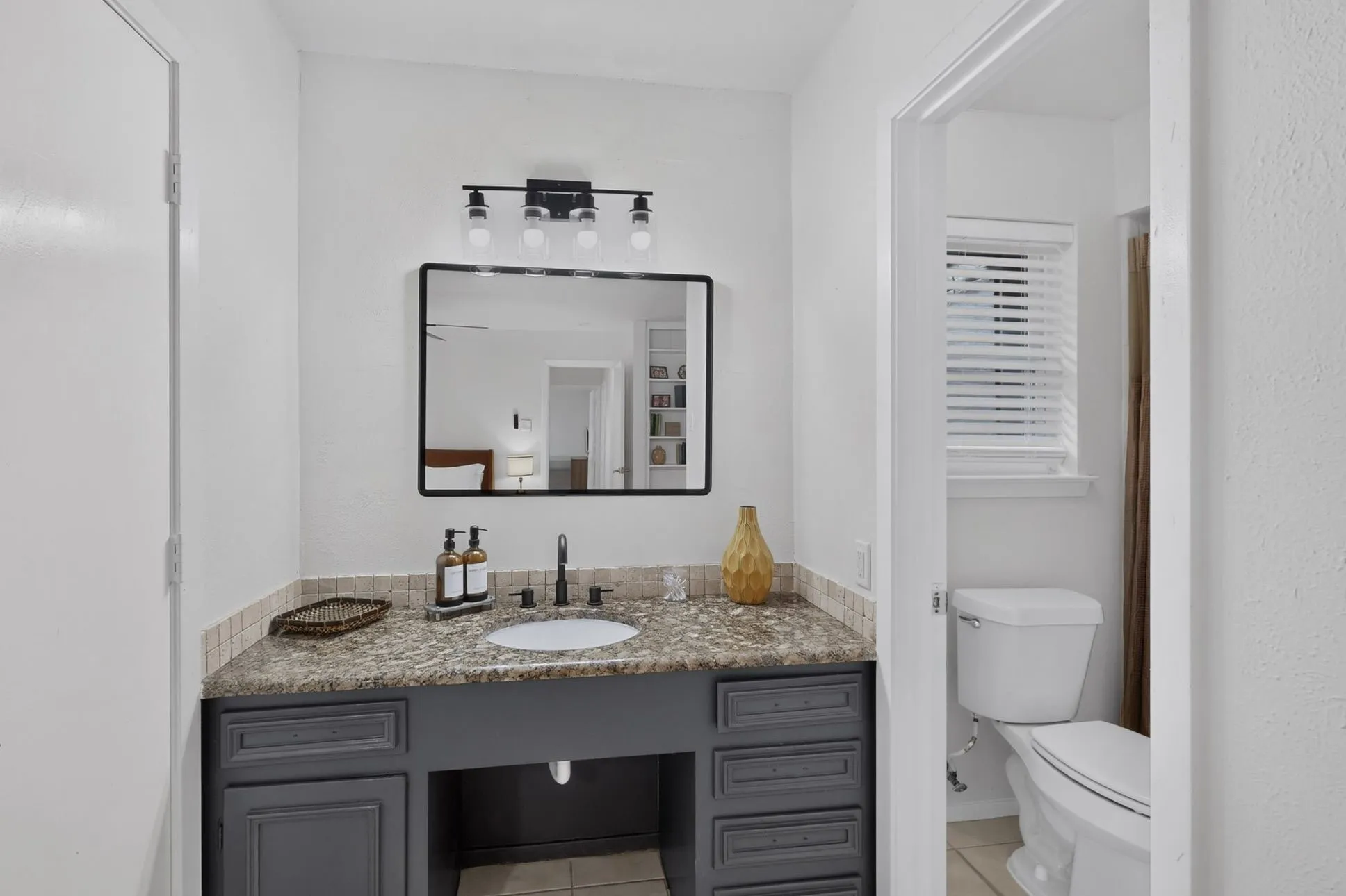 Bathroom vanity featuring a speckled countertop, undermount sink with a matte black faucet, and dark gray cabinetry