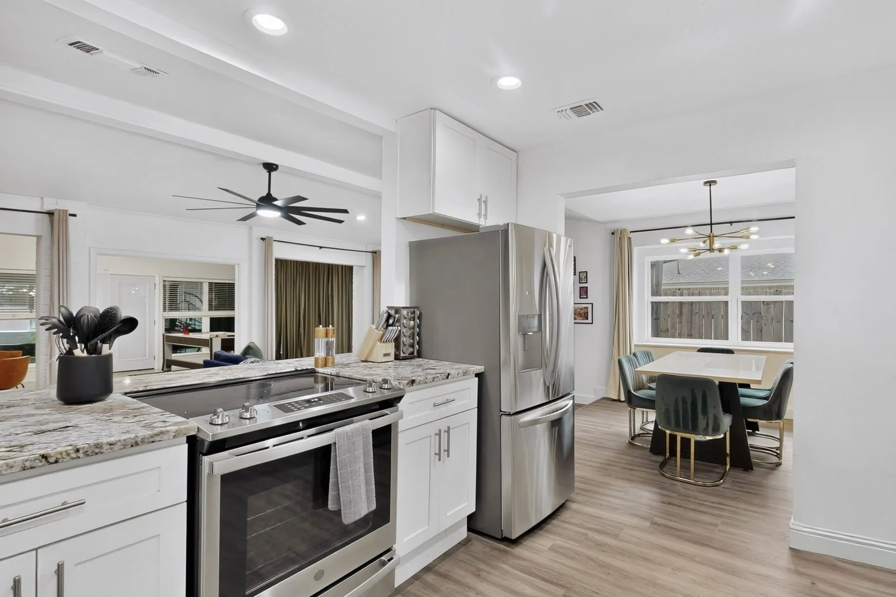 Modern kitchen featuring white cabinetry, stainless steel appliances, speckled stone countertops, and wood-finish flooring