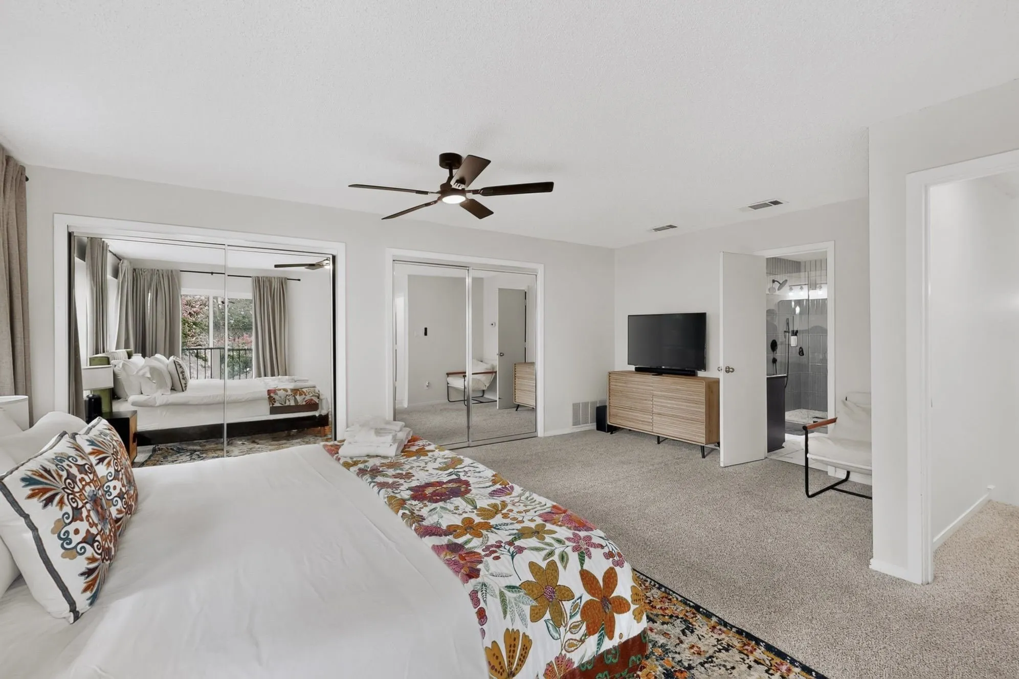 Spacious room featuring light-colored carpeting, a ceiling fan with integrated lighting, and multiple mirrored closet doors