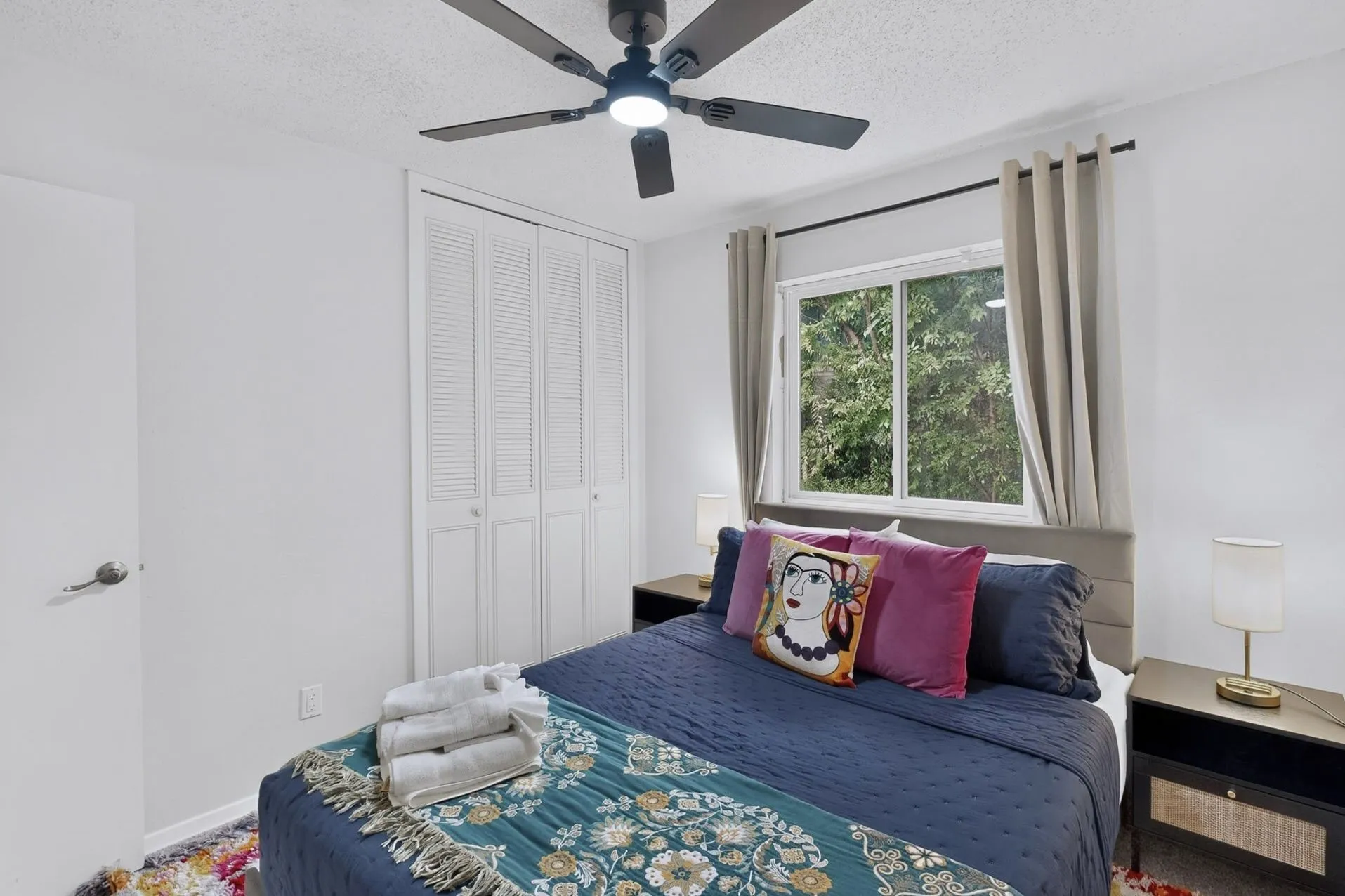 Bedroom featuring a window with exterior tree scenery, a ceiling fan with integrated lighting, and louvered bifold closet doors