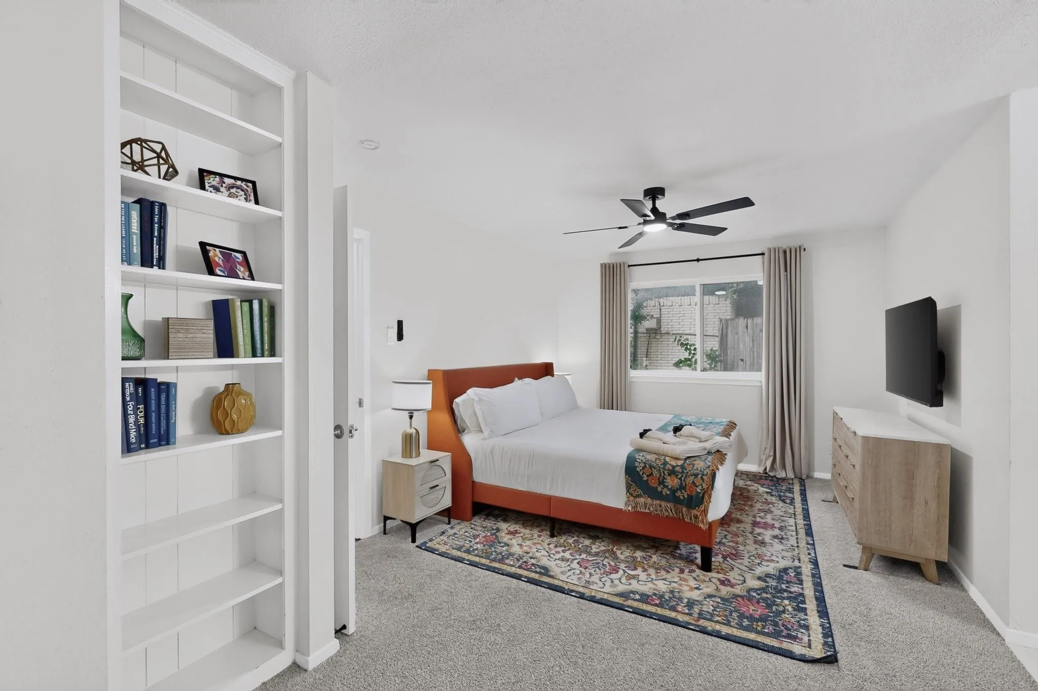 Bedroom featuring light gray carpeting, a multi-pane window with neutral drapes, and a ceiling fan with integrated lighting