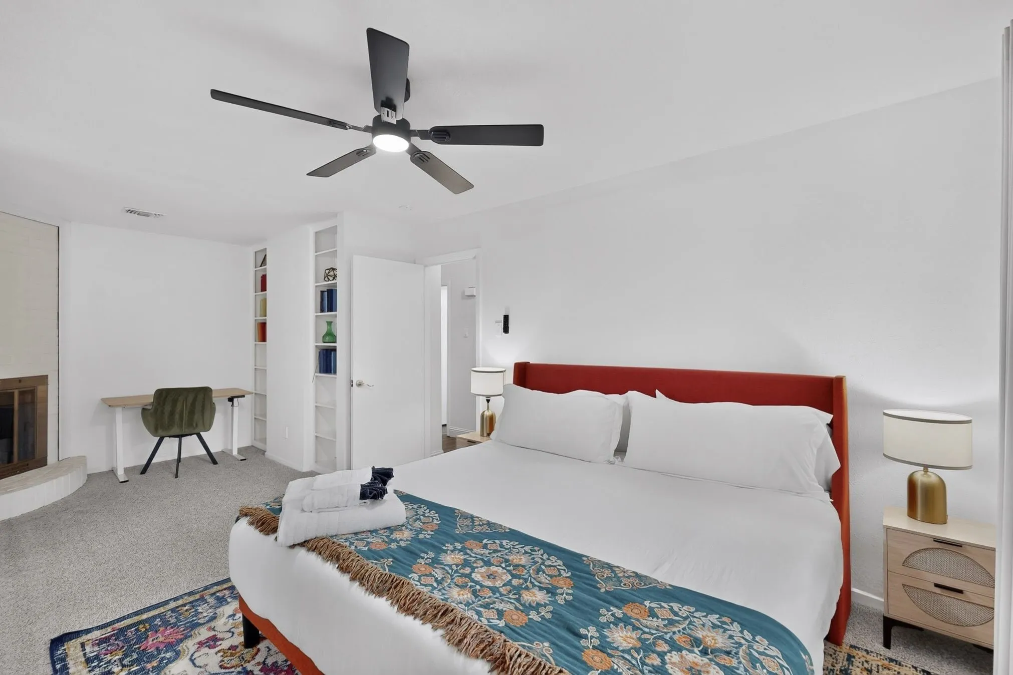 Carpeted bedroom featuring a ceiling fan with integrated lighting, a built-in shelving unit, and a fireplace with a hearth