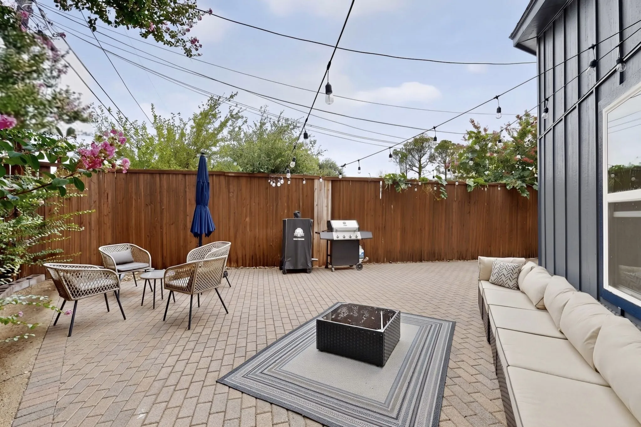 Paved patio featuring a privacy fence, string lighting, and board-and-batten siding