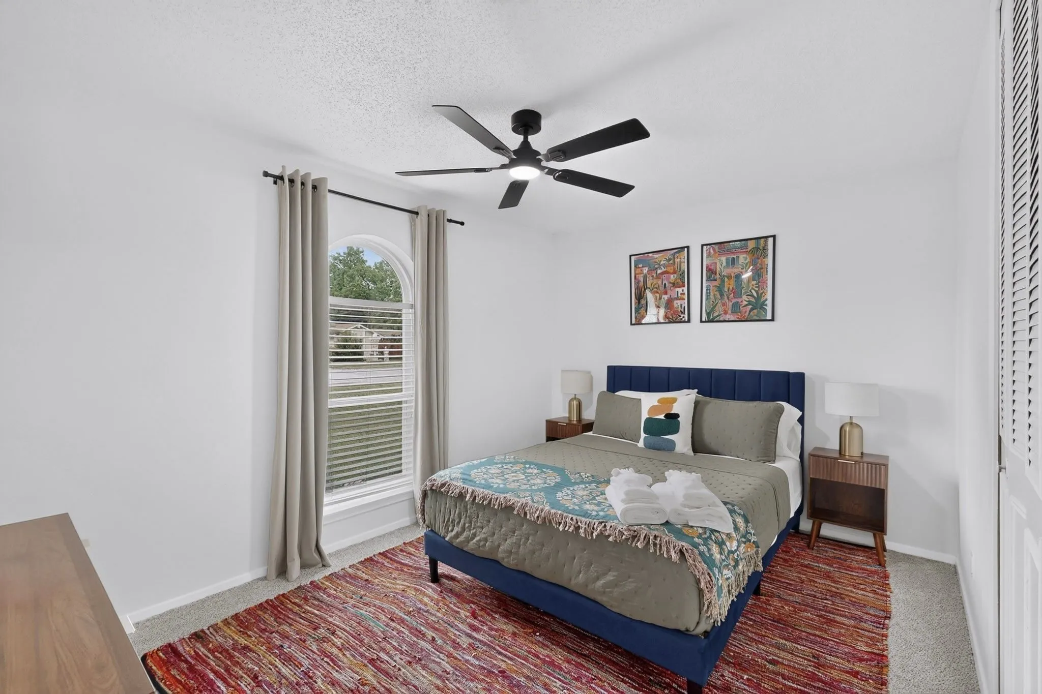 White-painted bedroom featuring a black ceiling fan, carpet flooring, and an arched window with blinds and drapes