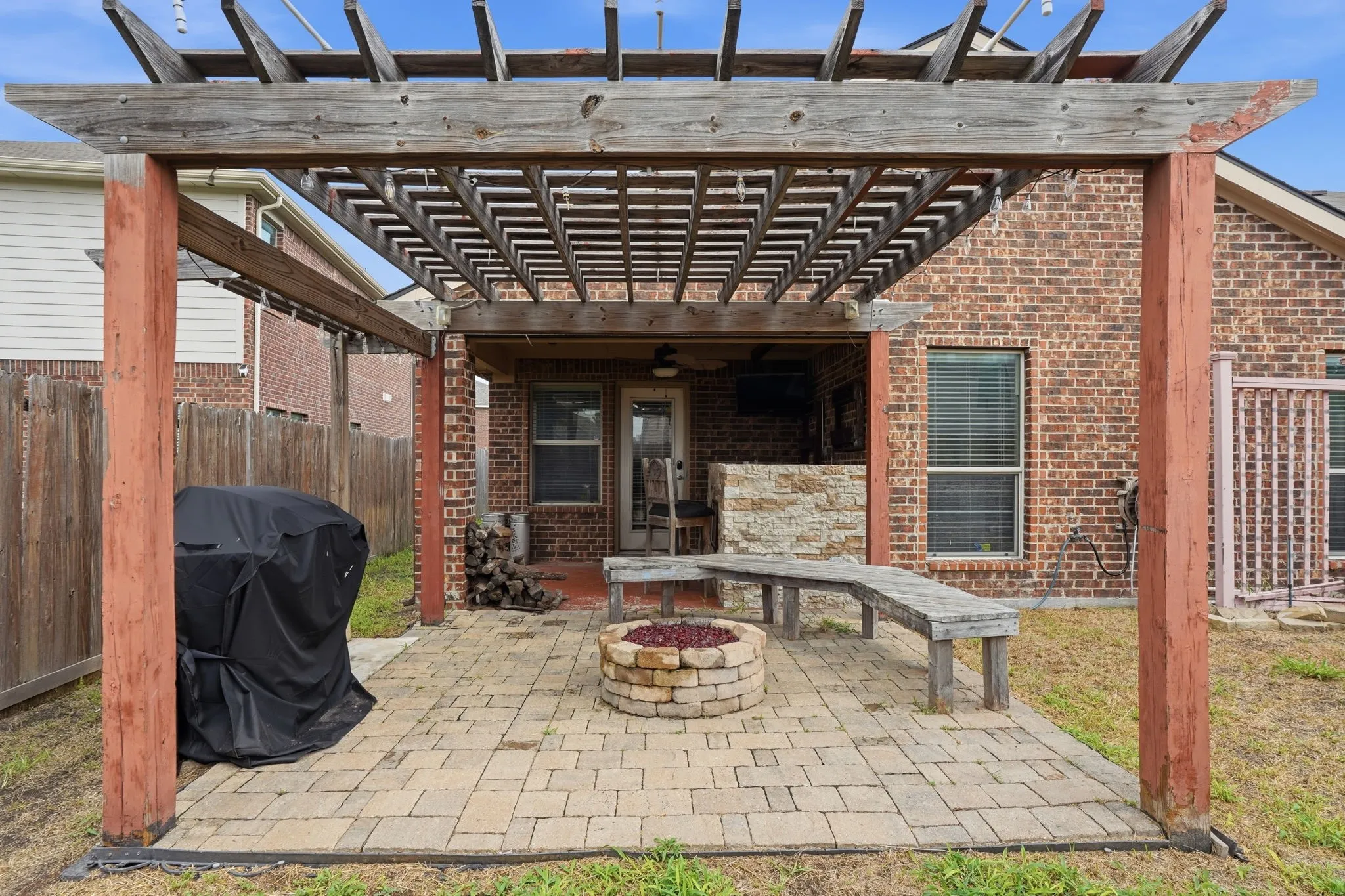 Patio area featuring a wood pergola, paver flooring, and a stone-clad fire pit