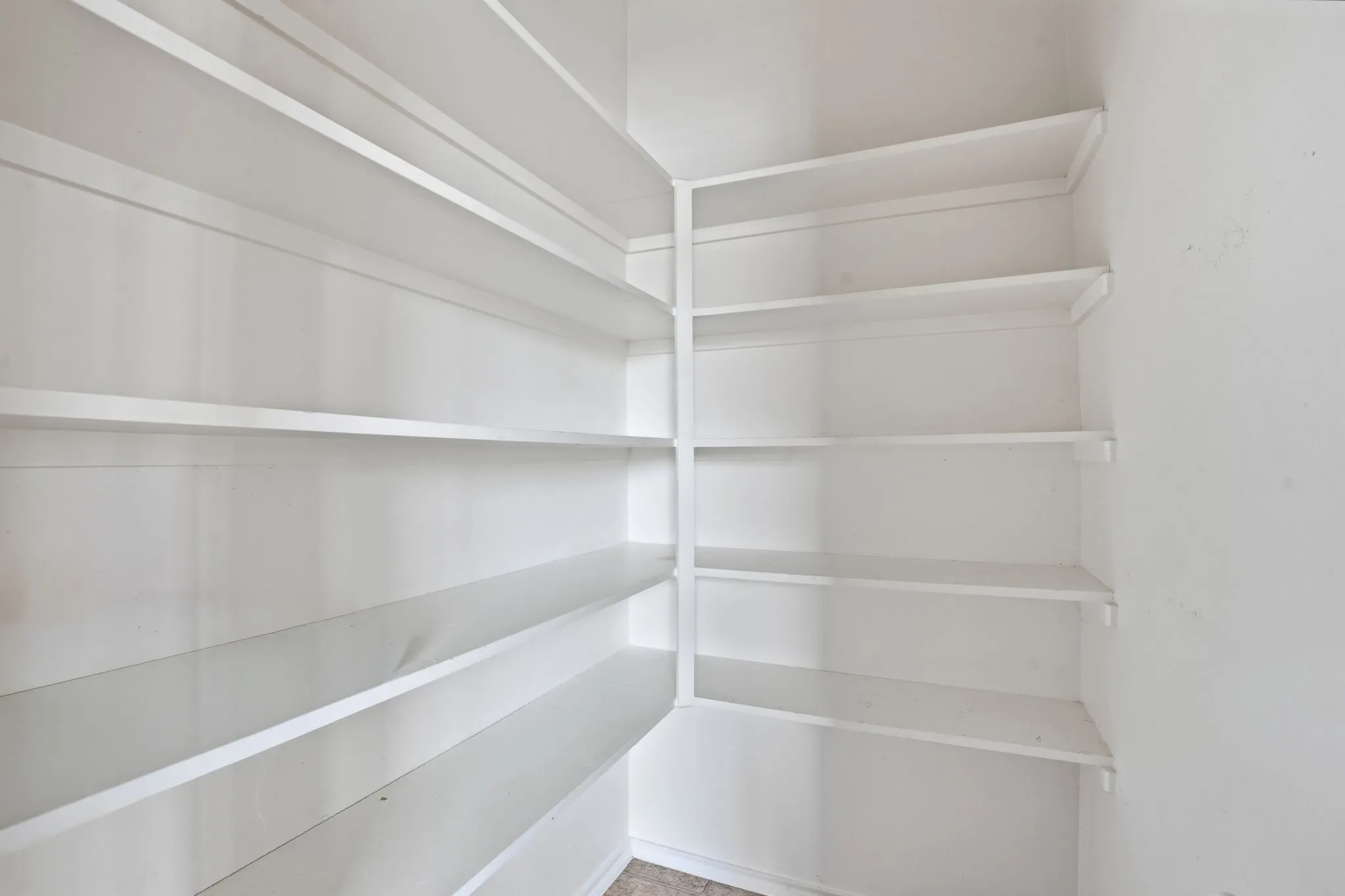 Corner pantry featuring multiple white shelves
