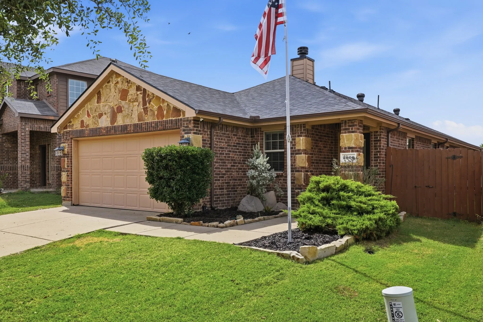 Brick and stone exterior featuring an attached two-car garage, concrete driveway, and a wood privacy fence
