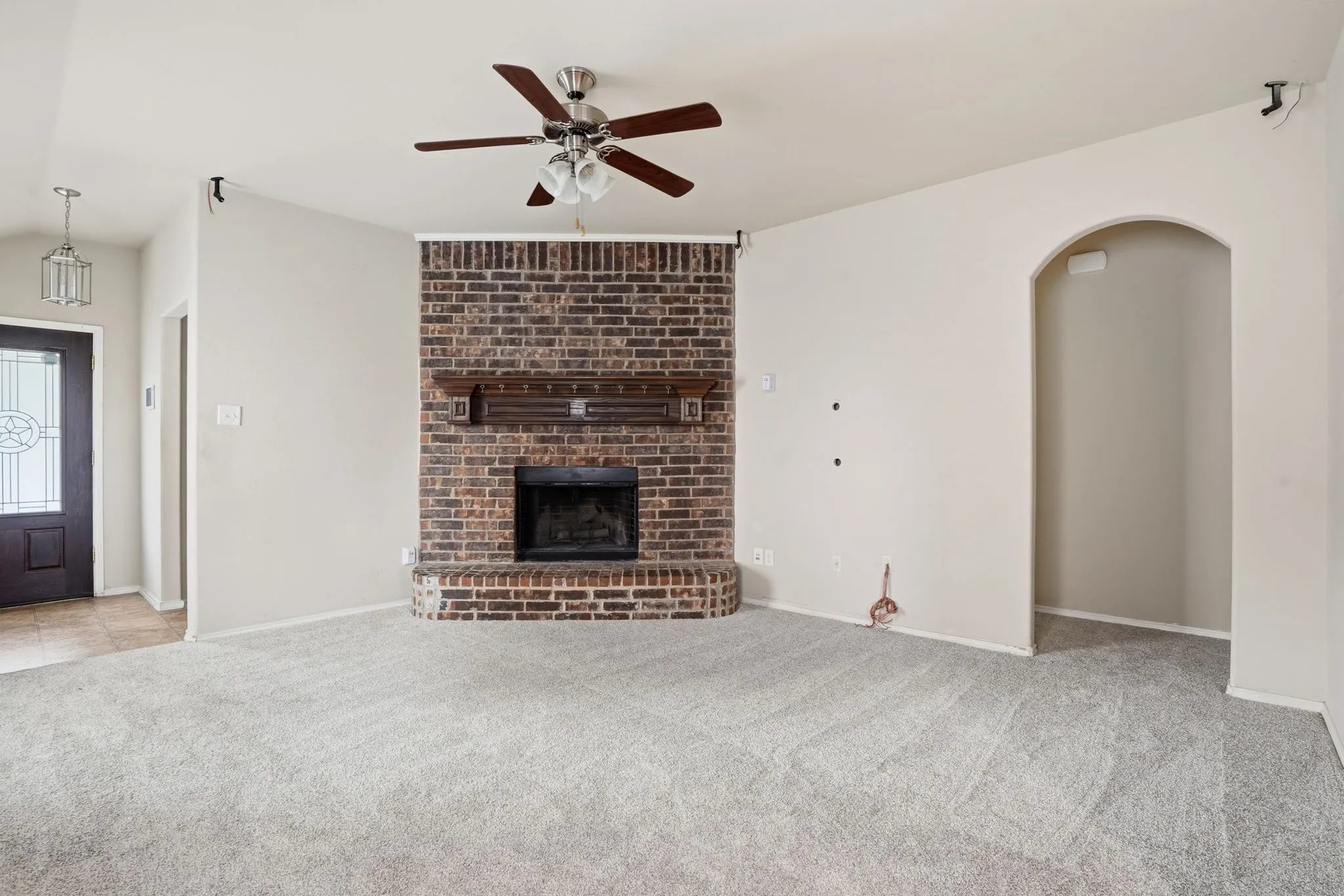 Living area featuring a brick fireplace with a wood mantle, light-toned carpeting, and a ceiling fan