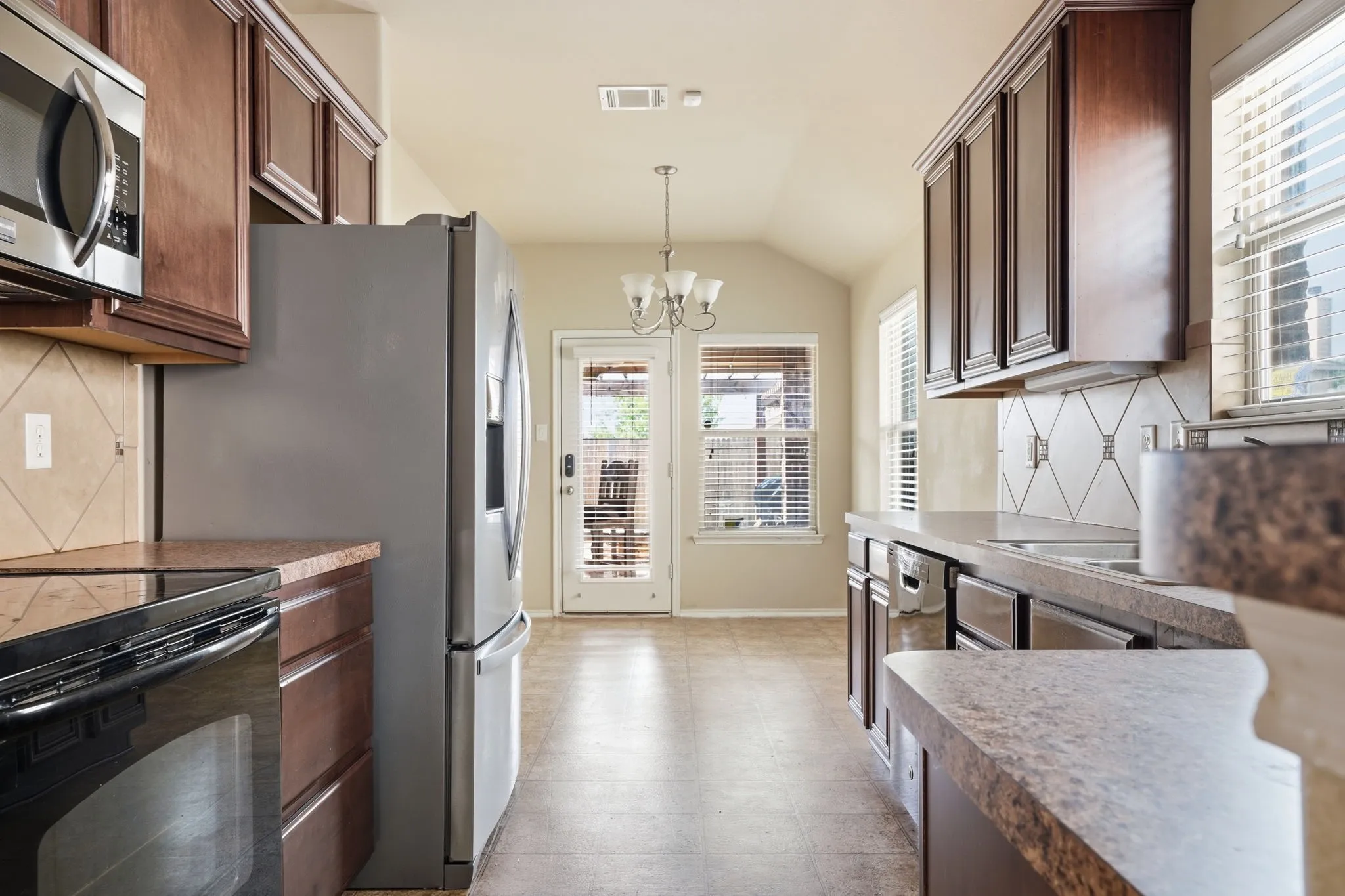 Kitchen featuring rich wood cabinetry, stainless steel appliances, a tile backsplash, and durable countertops