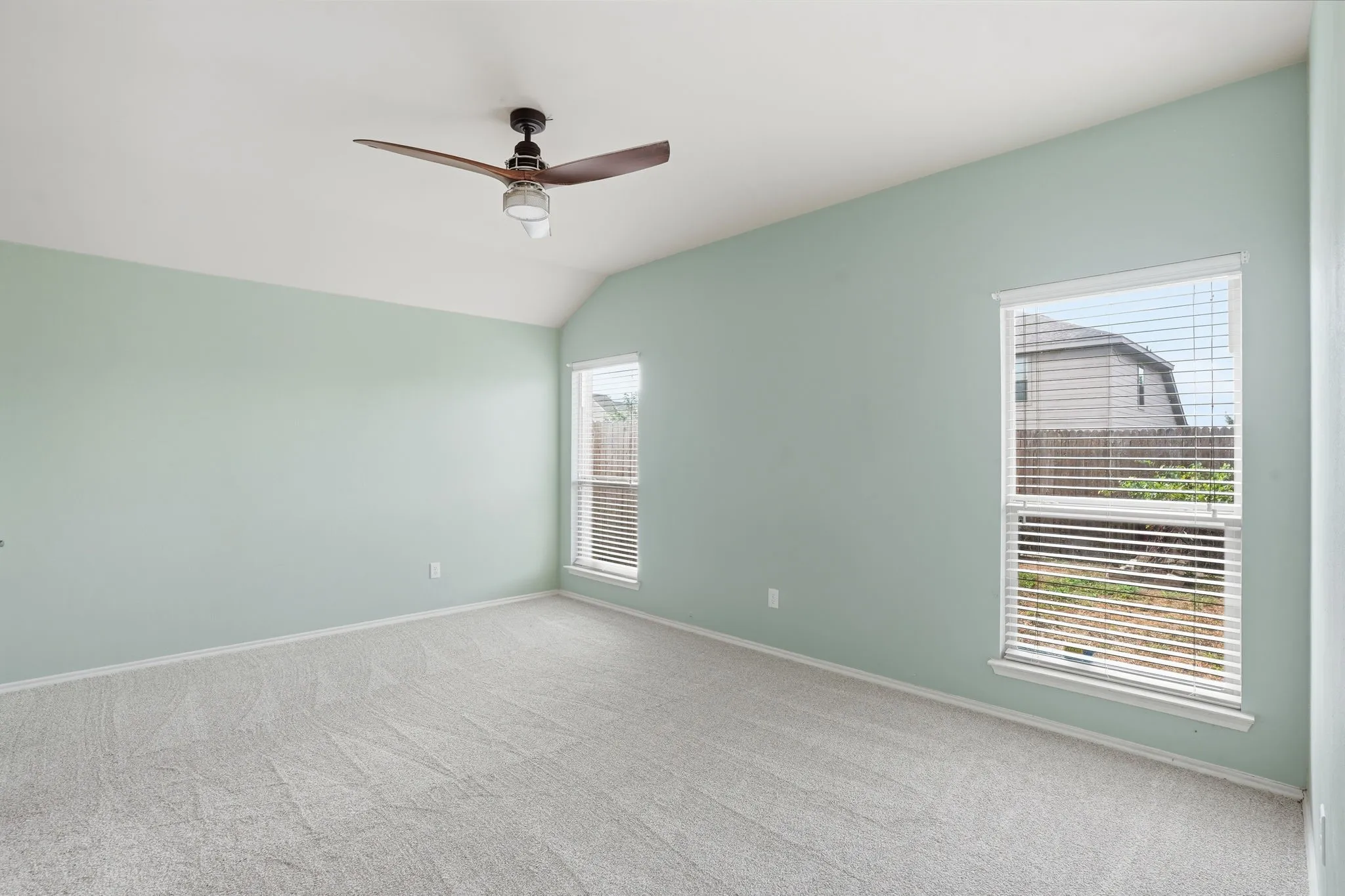 Spacious room featuring vaulted ceilings, light-toned carpeting, and pale green walls