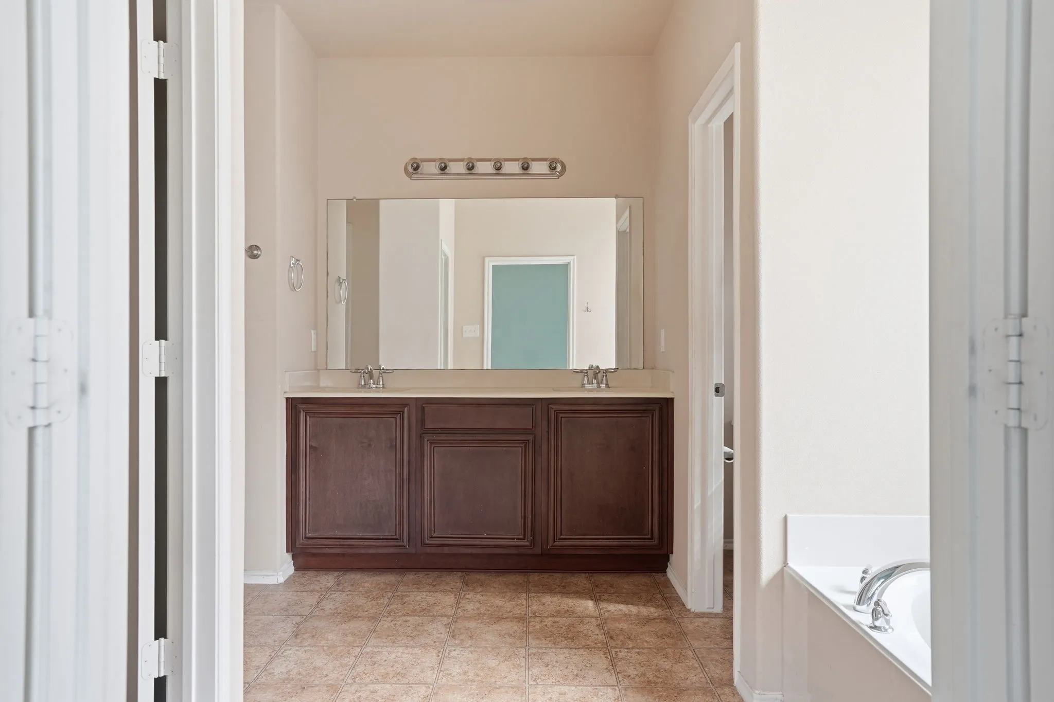 Bathroom vanity featuring a dual sink configuration with a large mirror, brown wood-finish cabinetry, and a light-colored countertop