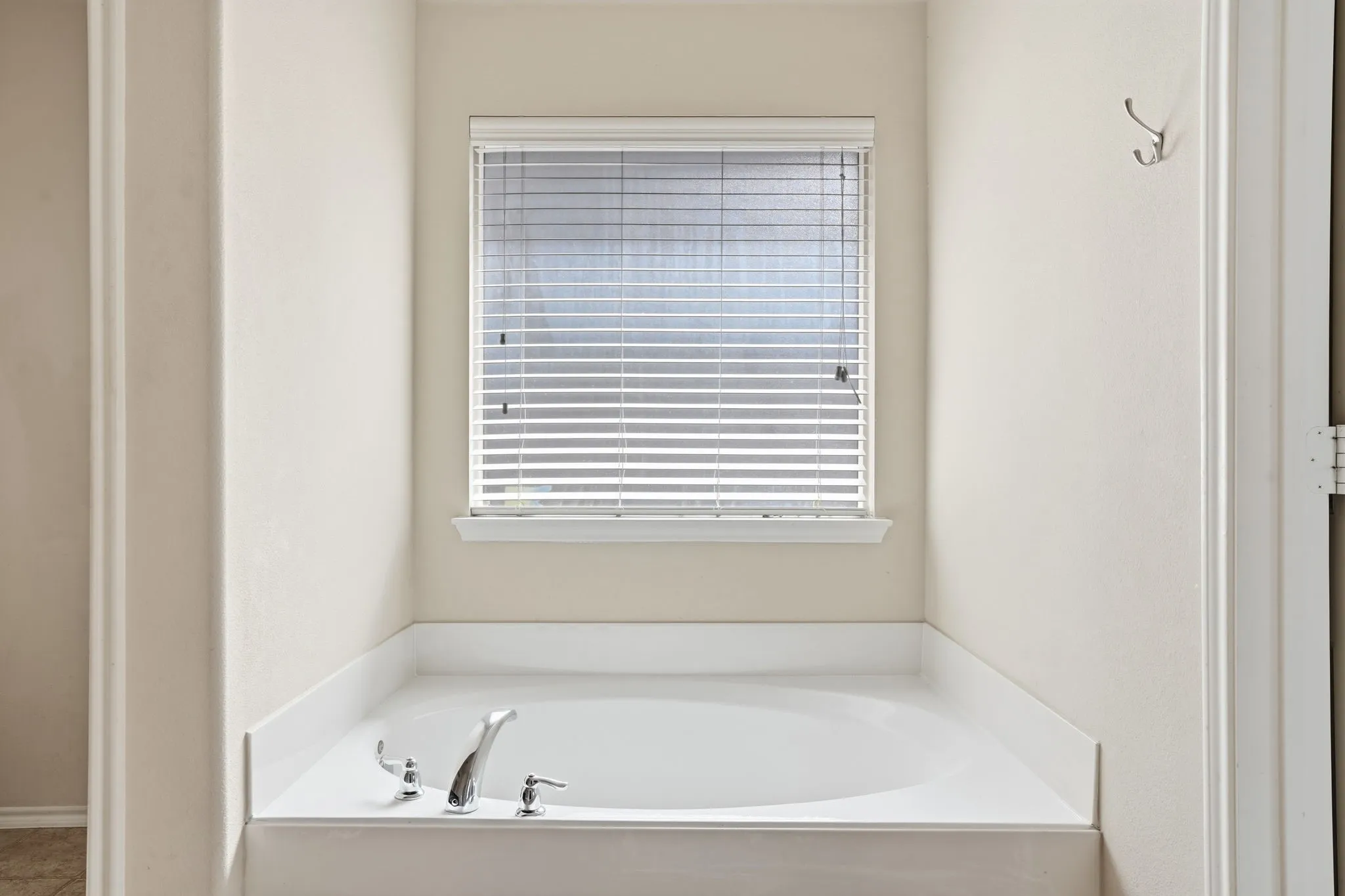 Soaking tub featuring chrome fixtures, a window with horizontal blinds, and a neutral wall palette
