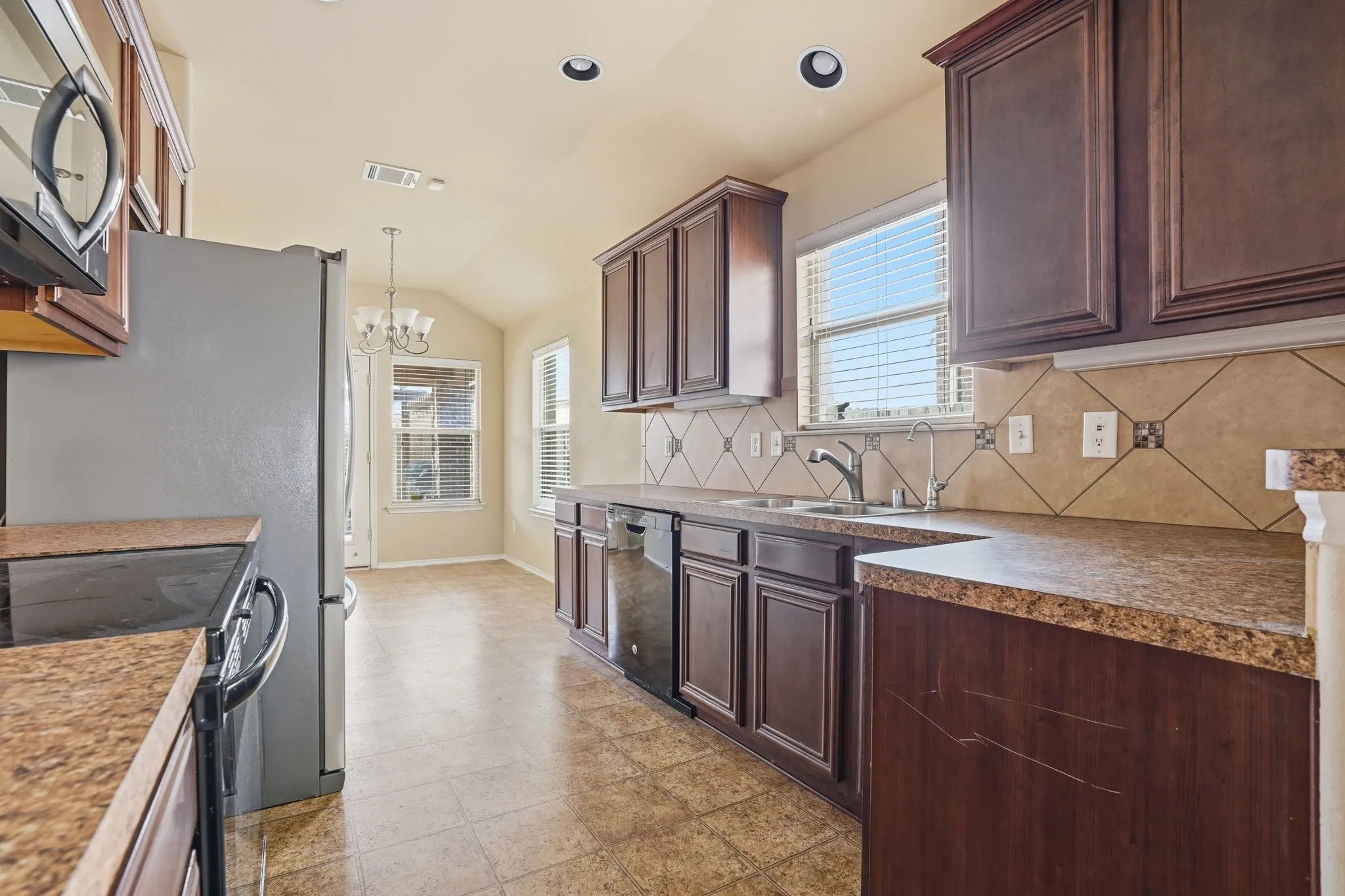 Functional kitchen featuring ample cabinetry, integrated stainless steel appliances, a double basin sink, and a tiled backsplash