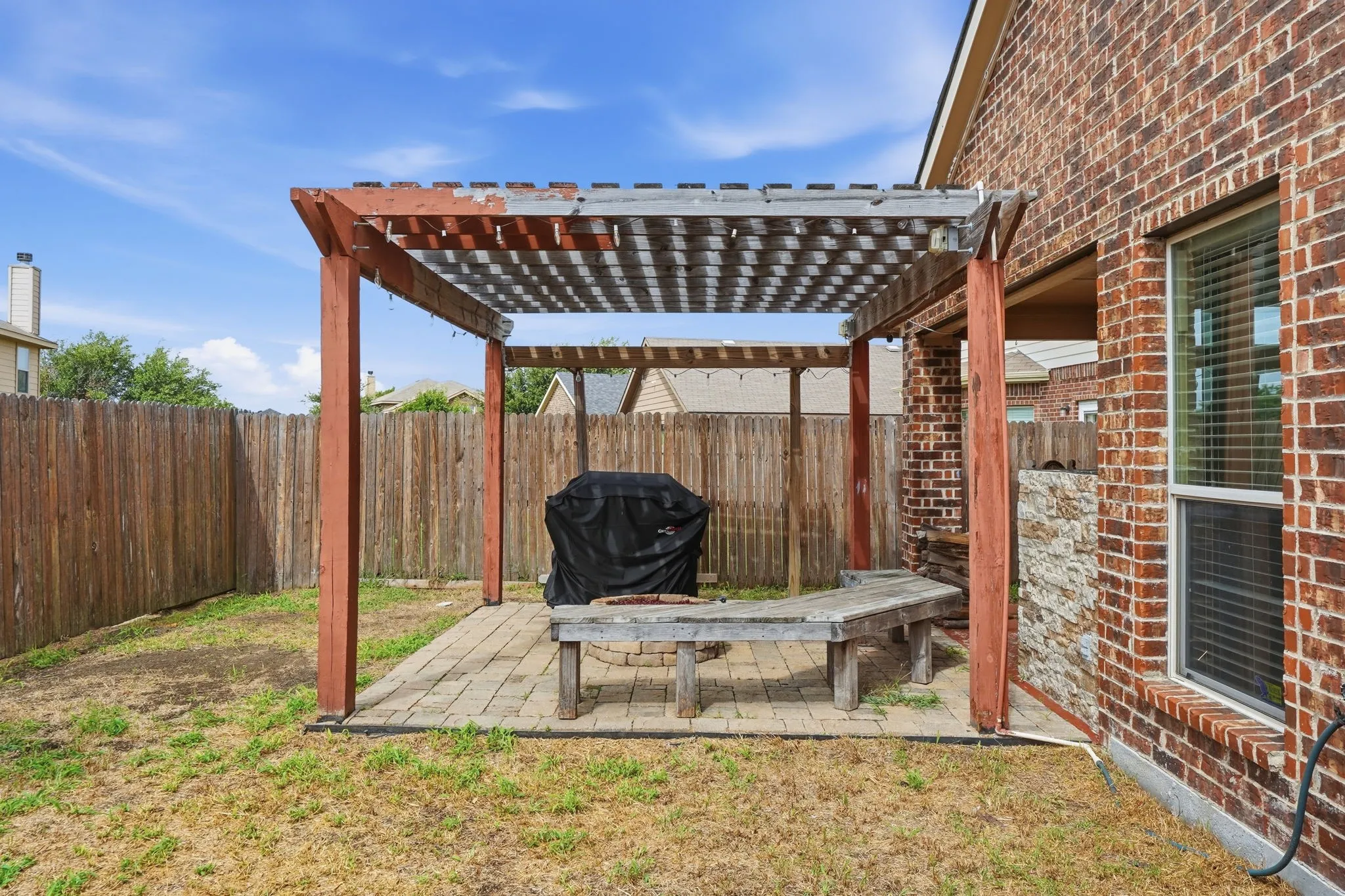 Paved patio featuring a wooden pergola with slatted cover, a built-in wooden bench, a stone-clad half-wall, and a brick exterior