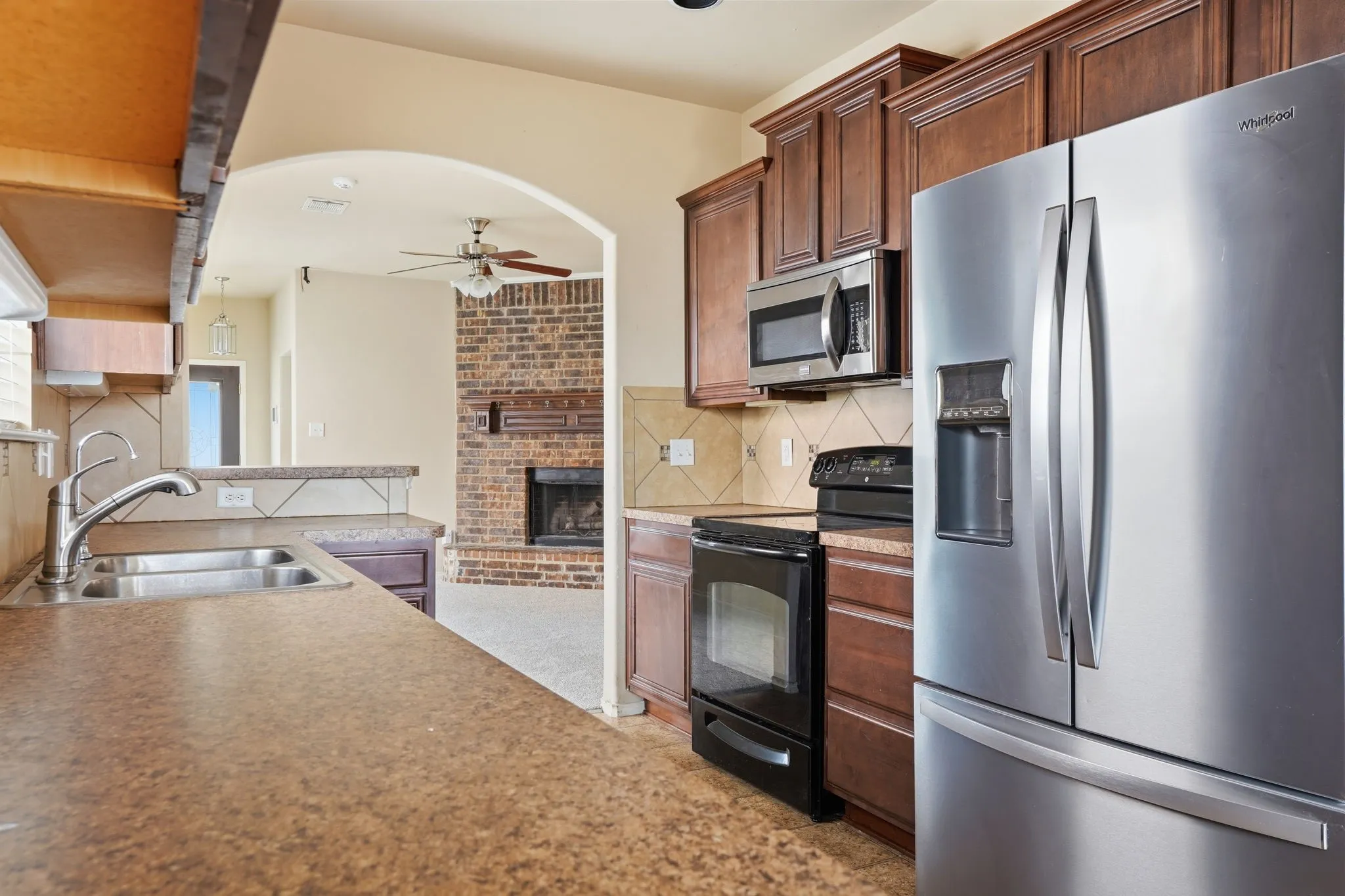 Kitchen featuring a double basin stainless steel sink, dark wood cabinetry, stainless steel refrigerator, stainless steel microwave, and a tiled backsplash