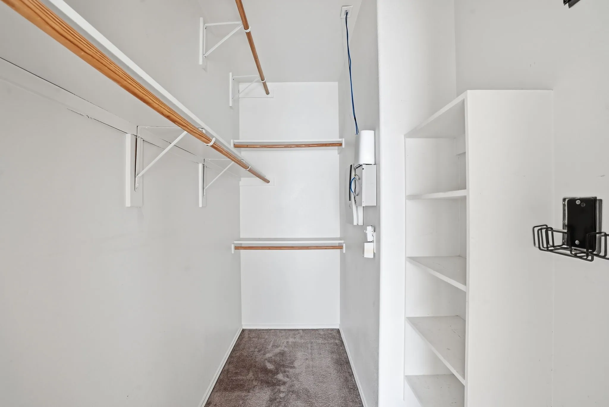 Walk-in closet featuring two levels of wood-finish hanging rods, white shelving units, and carpet flooring