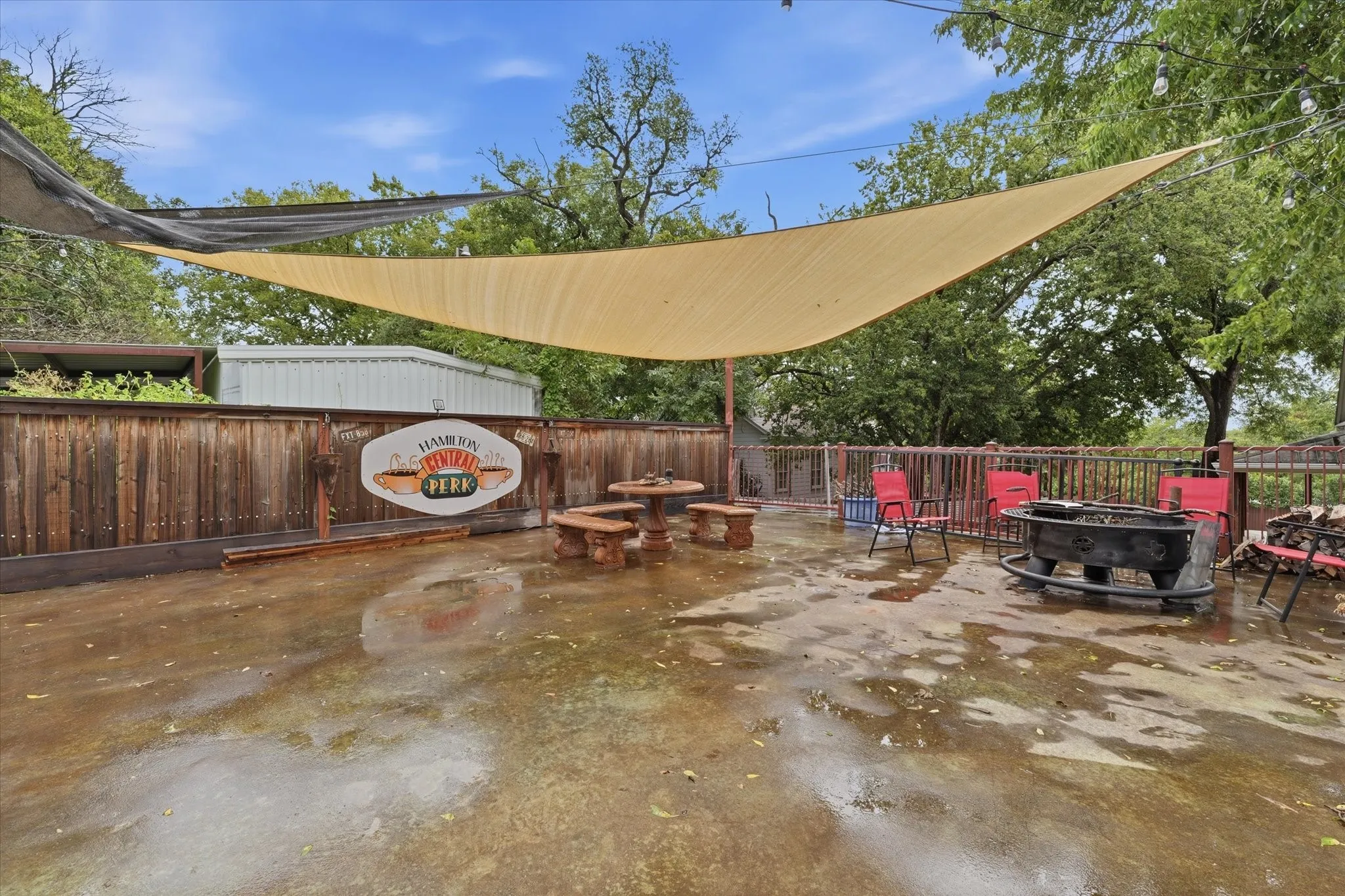 Spacious outdoor patio area featuring a concrete surface, a privacy fence, a firepit, and multiple shade sails