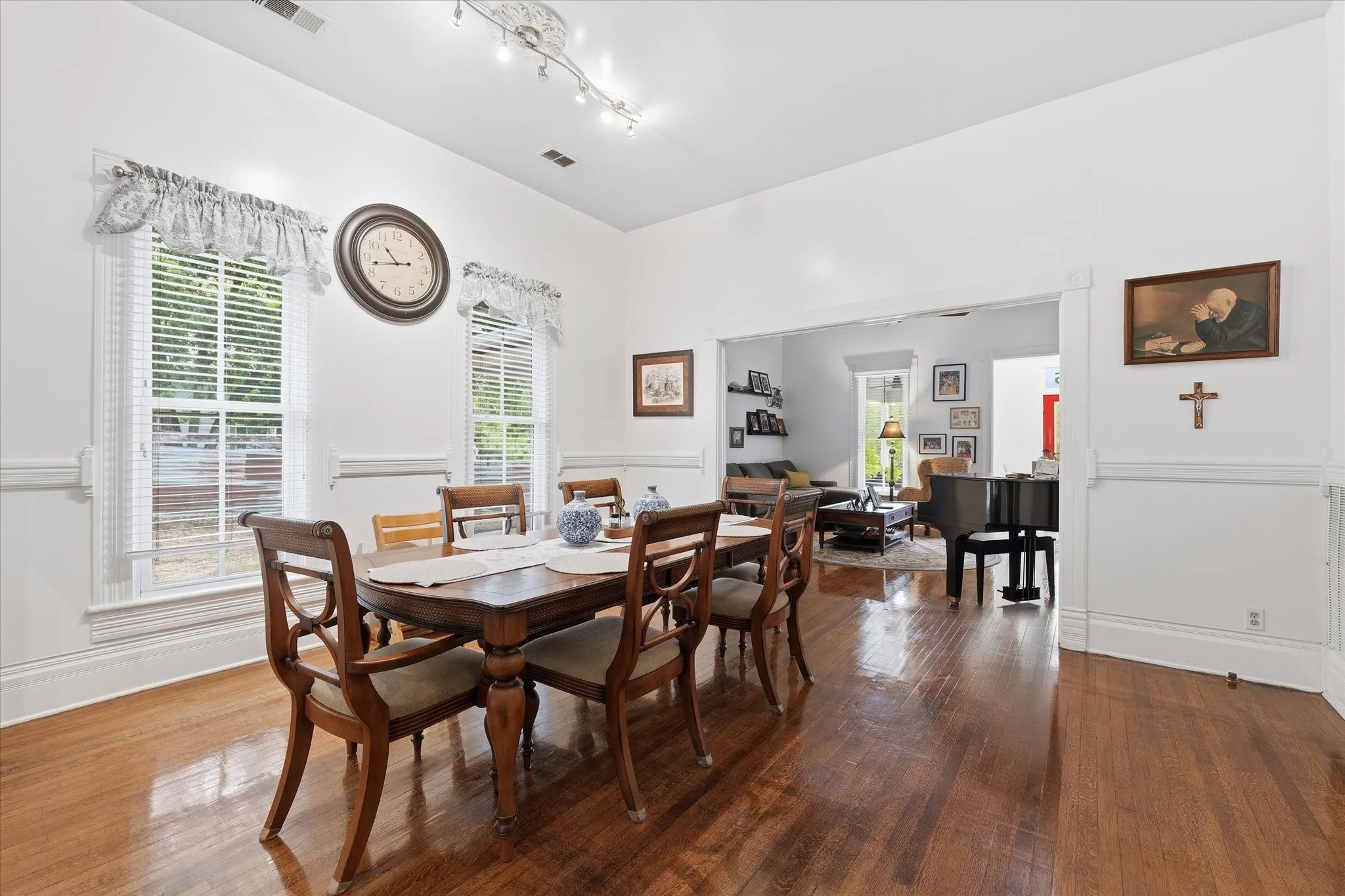Spacious dining area featuring rich oak hardwood flooring, white walls with custom trim and chair rail, and two large windows