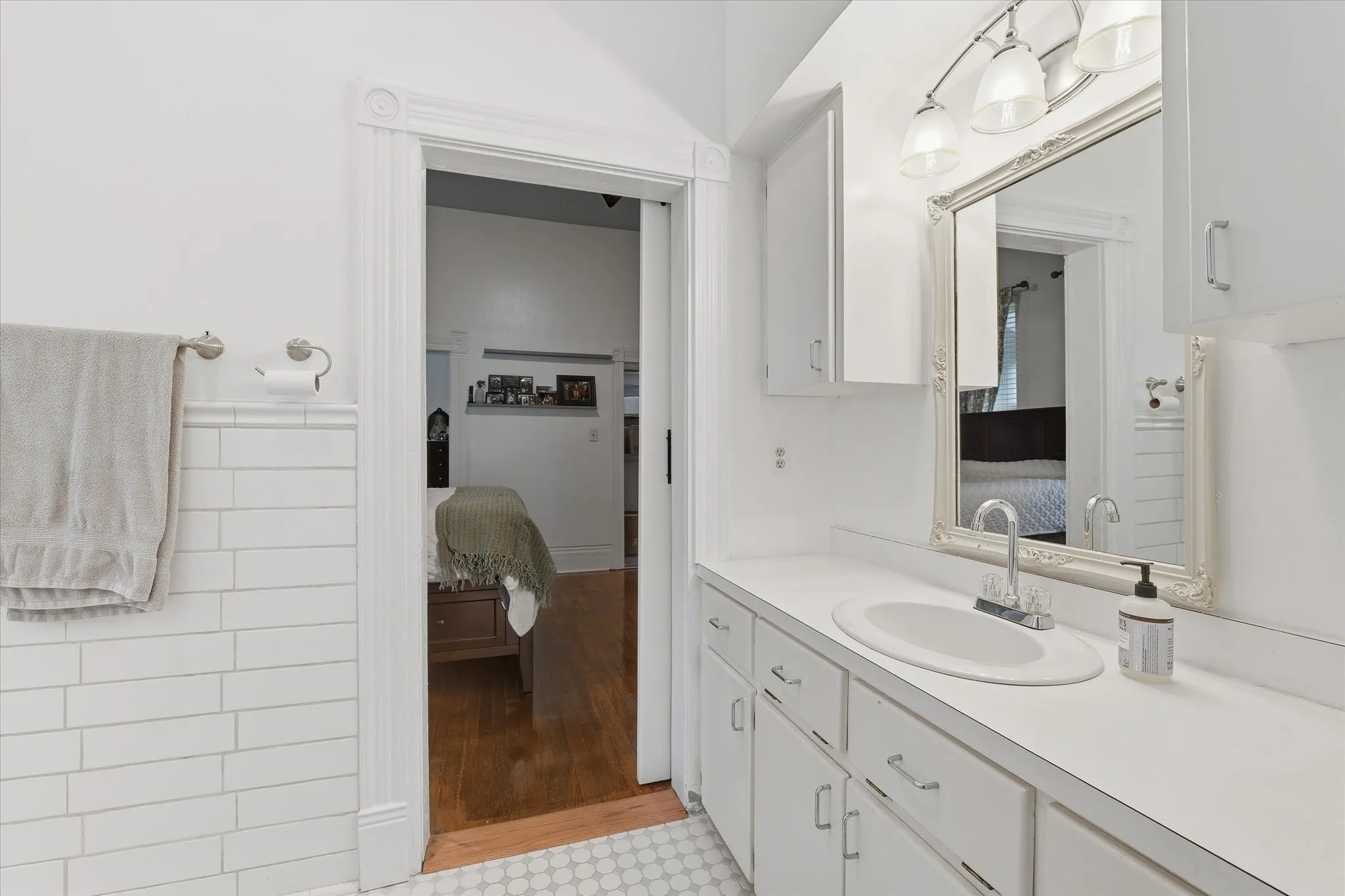 Jack-and-Jill bathroom featuring a vanity with a white countertop and integrated sink, a large framed mirror, and white cabinetry