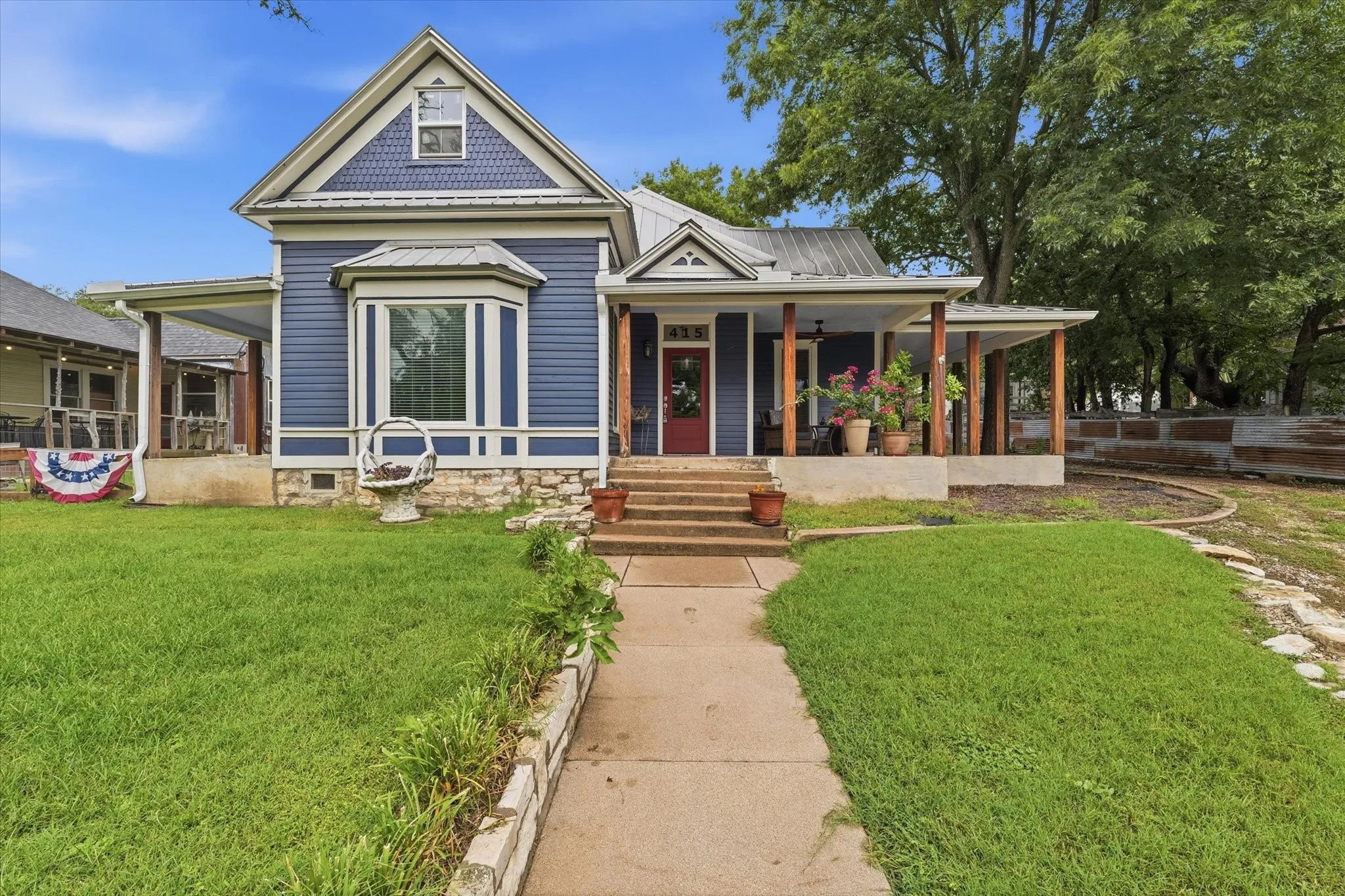 Blue siding exterior featuring a prominent bay window with white trim, a covered front porch with wood columns, and a red entry door