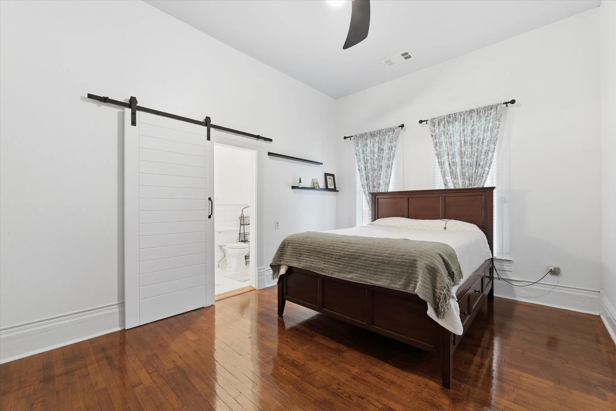 Hardwood flooring featuring white walls, a barn-style sliding door, ceiling fan, and closet