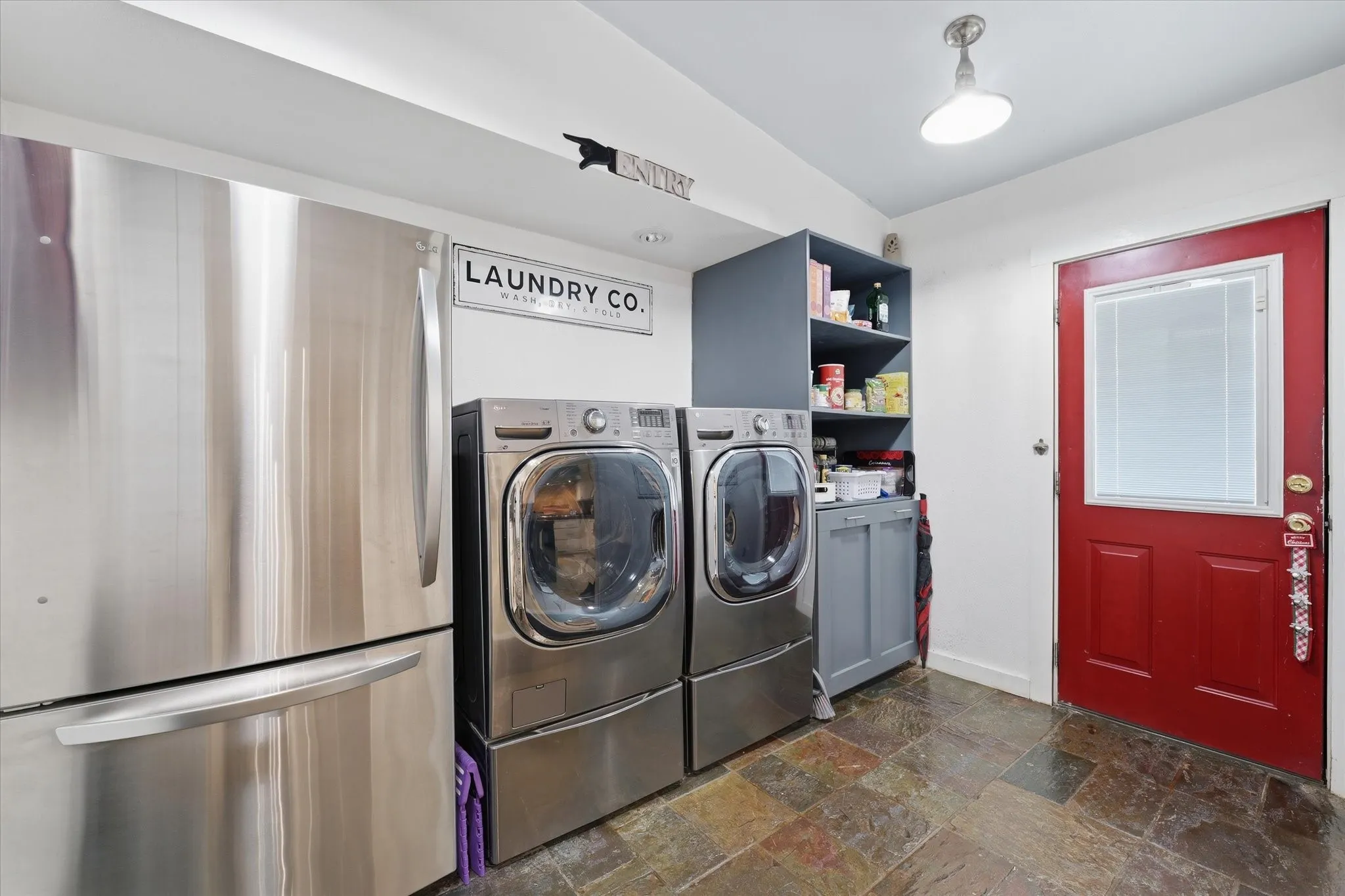 Utility space featuring multi-toned slate tile flooring, a red door with an integrated mini-blind, and built-in pantry with lower cabinetry